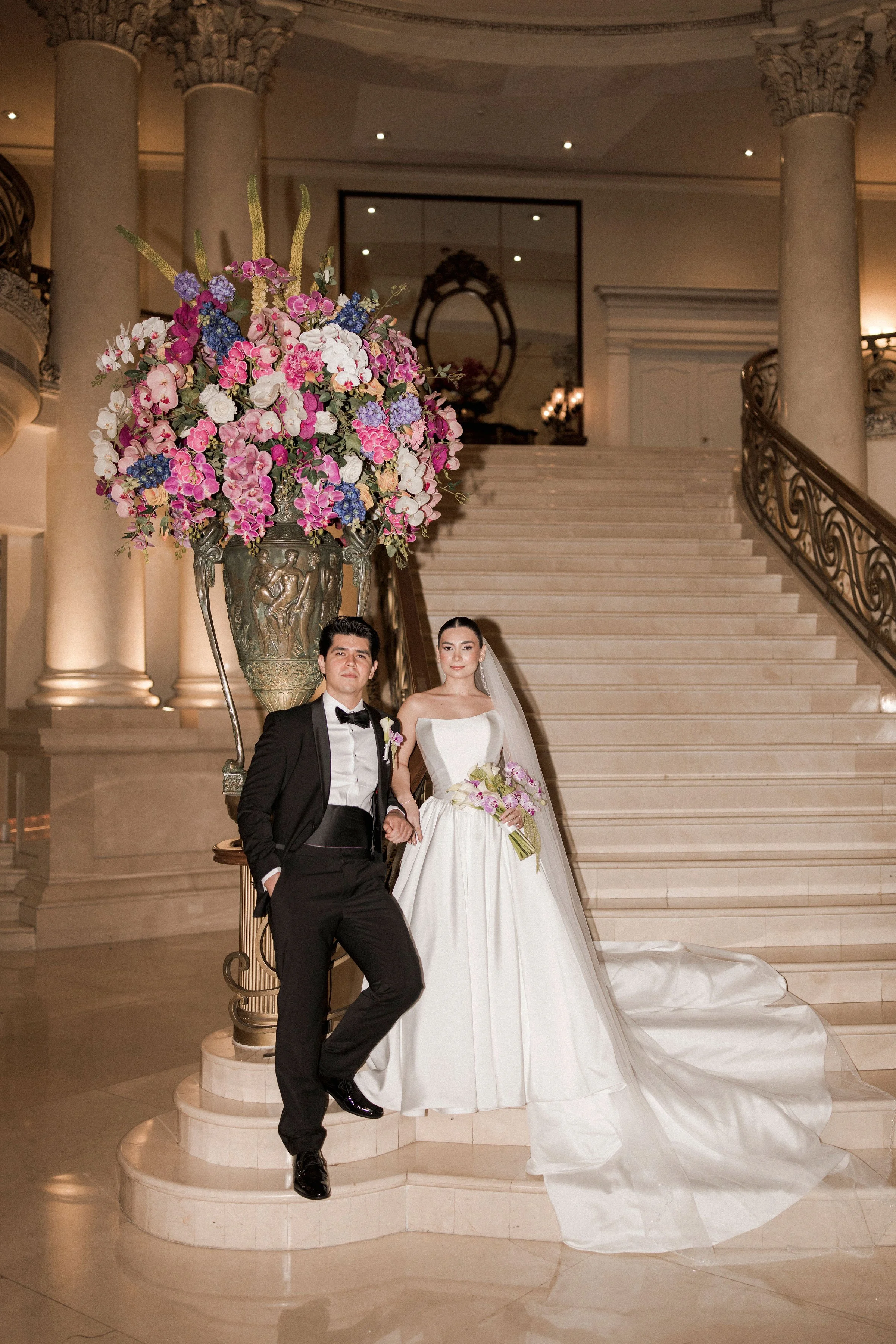 Novios bajo una instalación floral rosa mientras la novia sostiene su ramo