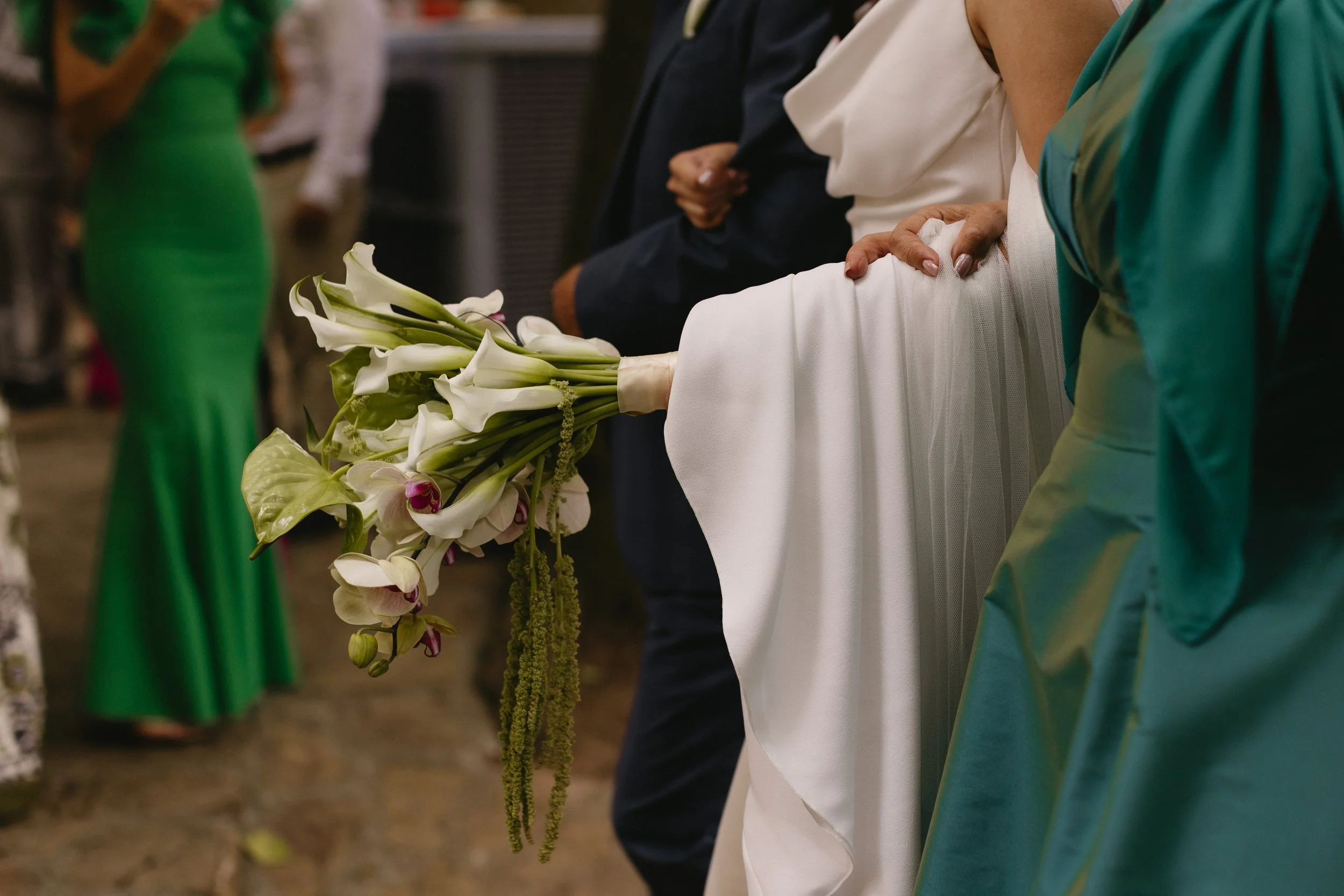 Novia sosteniendo un ramo alargado de flores blancas, follaje verde y amaranto colgante