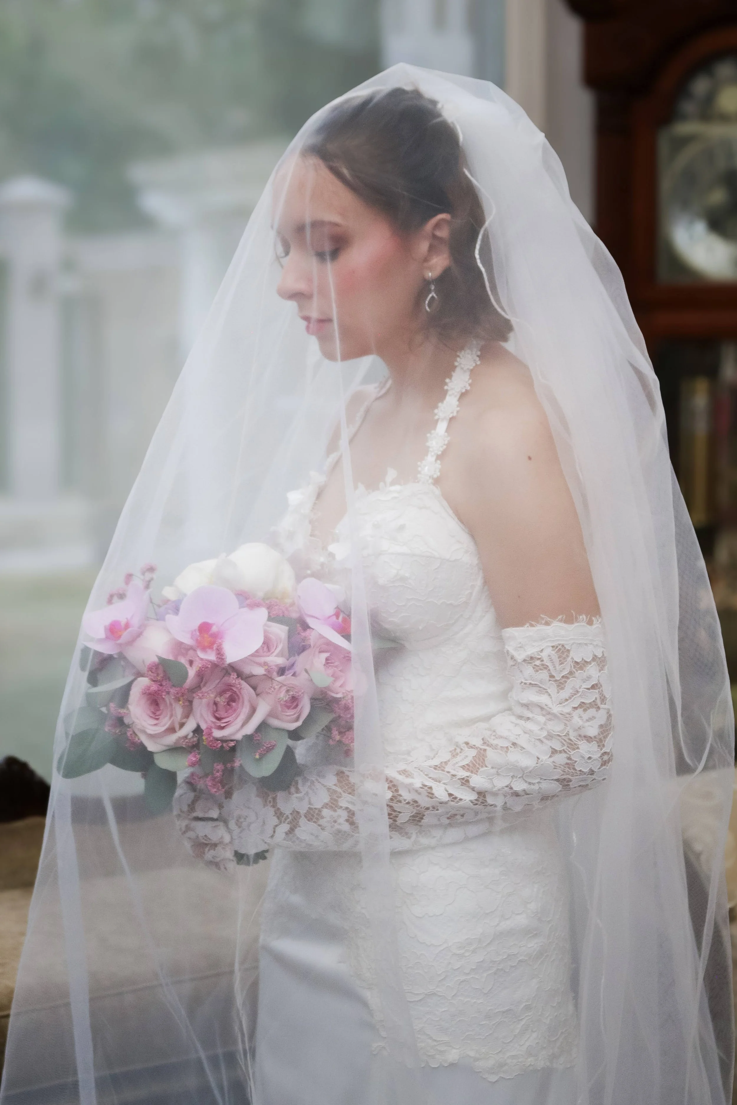 Novia bajo el velo sosteniendo un ramo clásico de orquídeas y rosas en tonos rosa