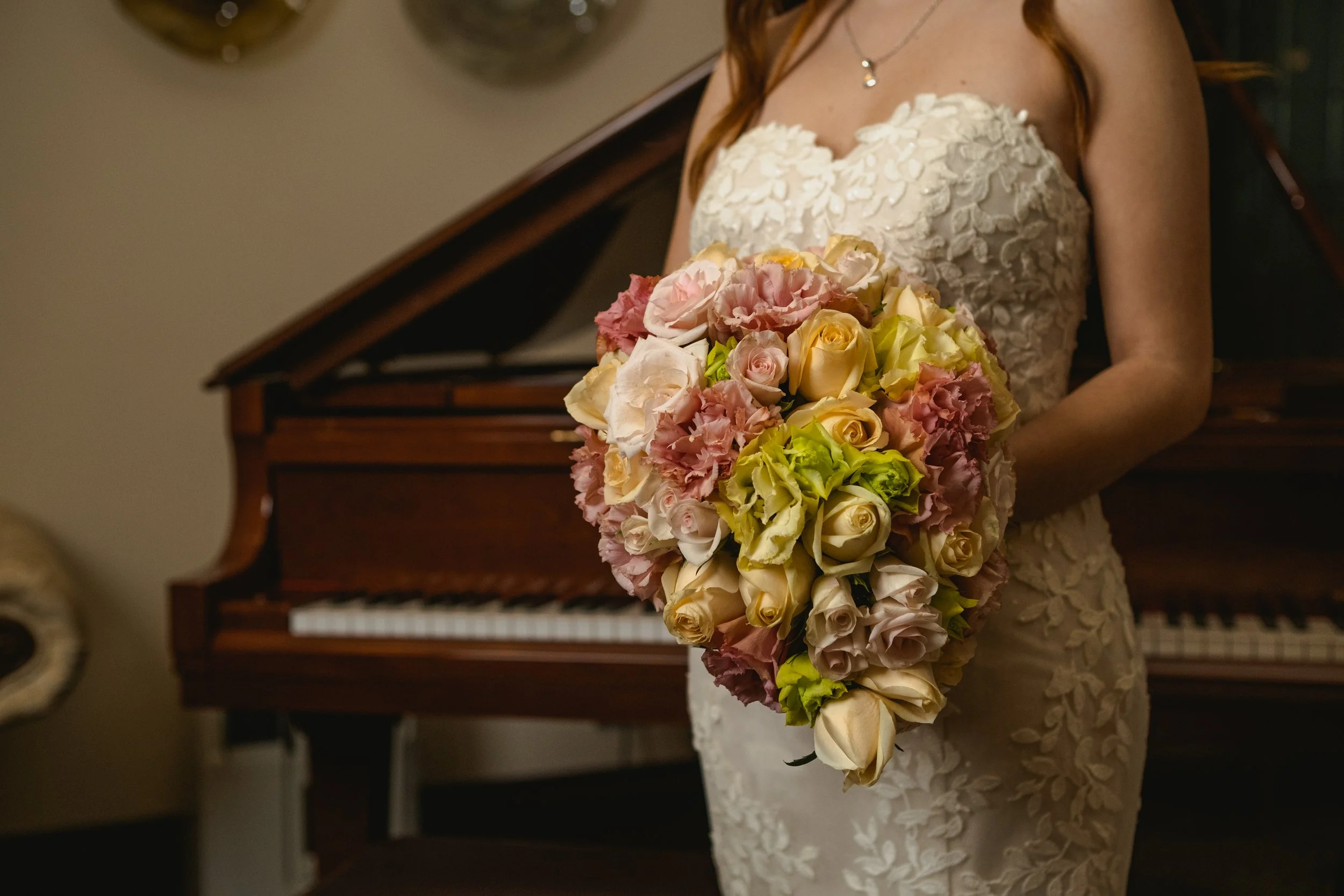 Novia sosteniendo un ramo con caída en tonos rosa, amarillo y verde junto a un piano