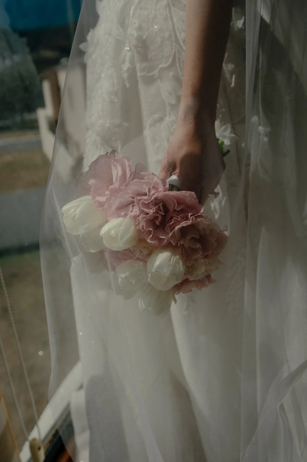 Novia sosteniendo un ramo clásico de tulipanes blancos y claveles rosa pastel bajo el velo