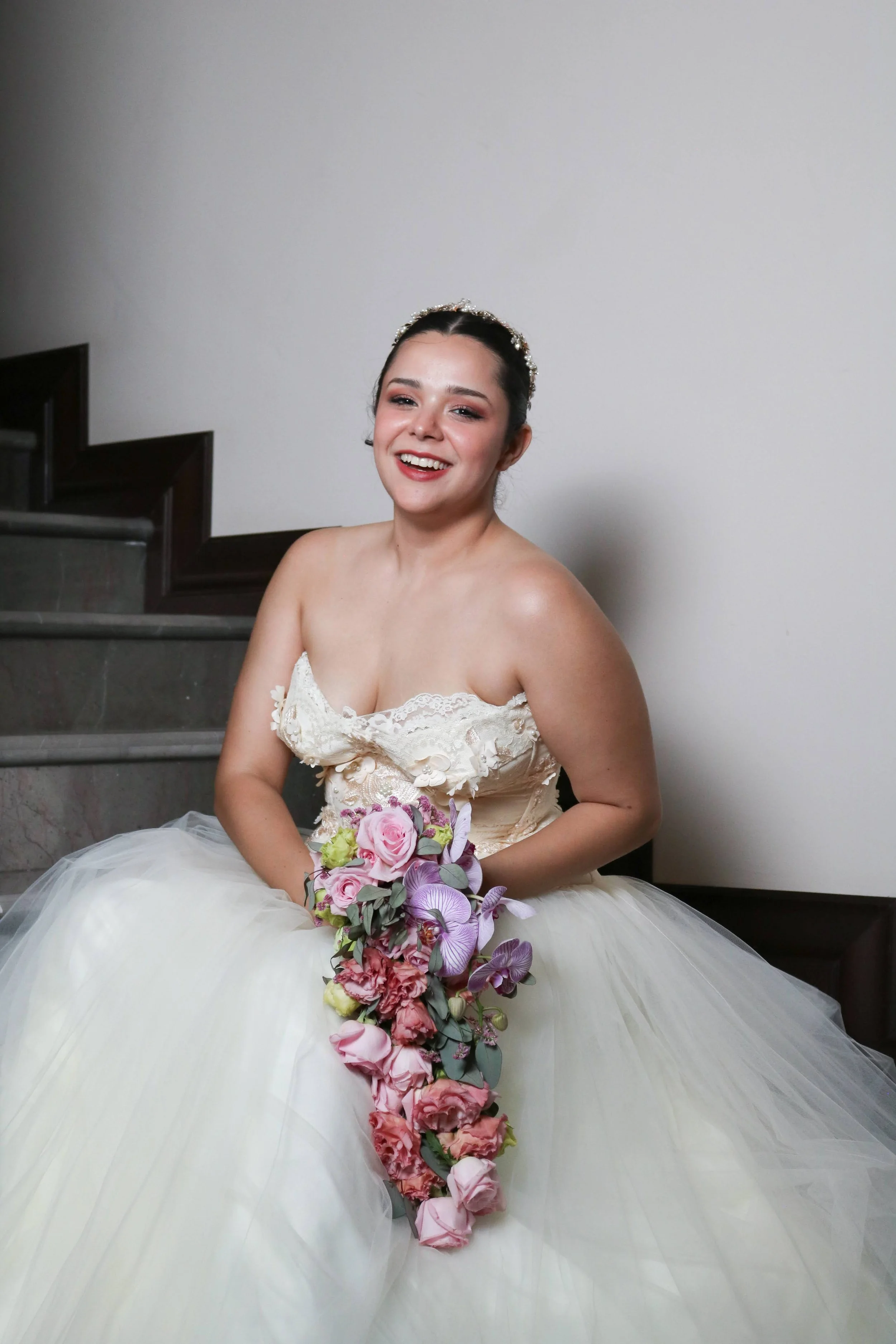 Novia sentada sonriendo con un ramo en cascada en tonos rosa y morado