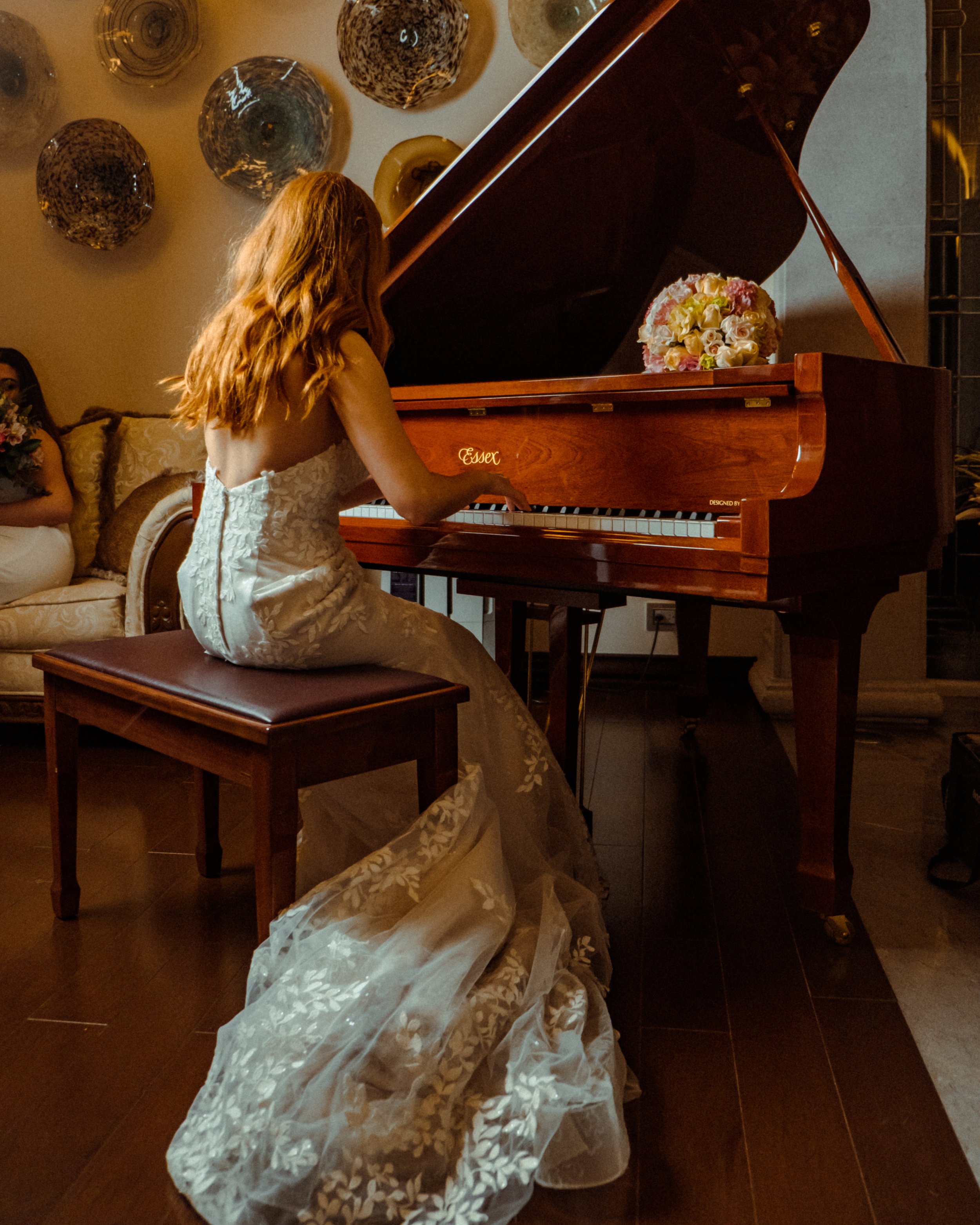 Novia sentada frente a un piano junto a un ramo de novia con caída