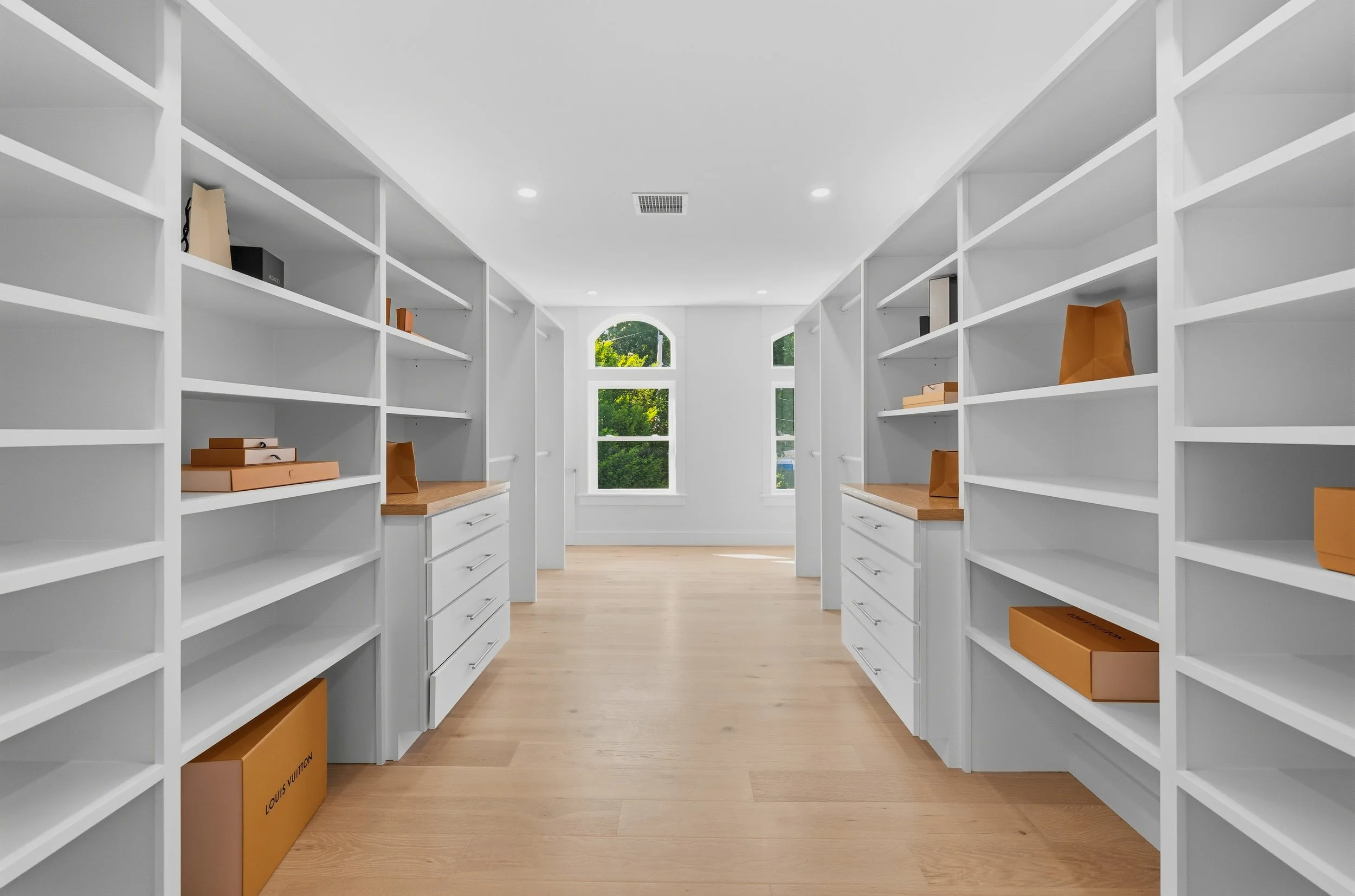 Empty white bookshelf units with a few boxes and folders, a window with greenery outside, and a clear ceiling with bright lighting.