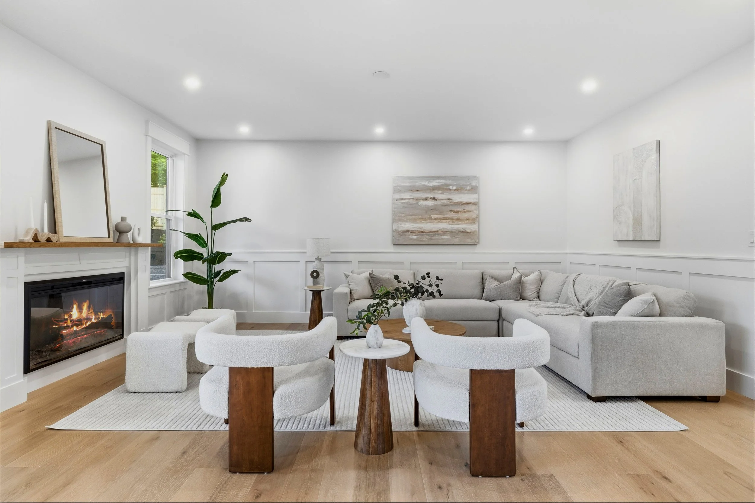 Bright, modern living room with a white sectional sofa, a fireplace, abstract art on the walls, a large window, and minimalist decor.