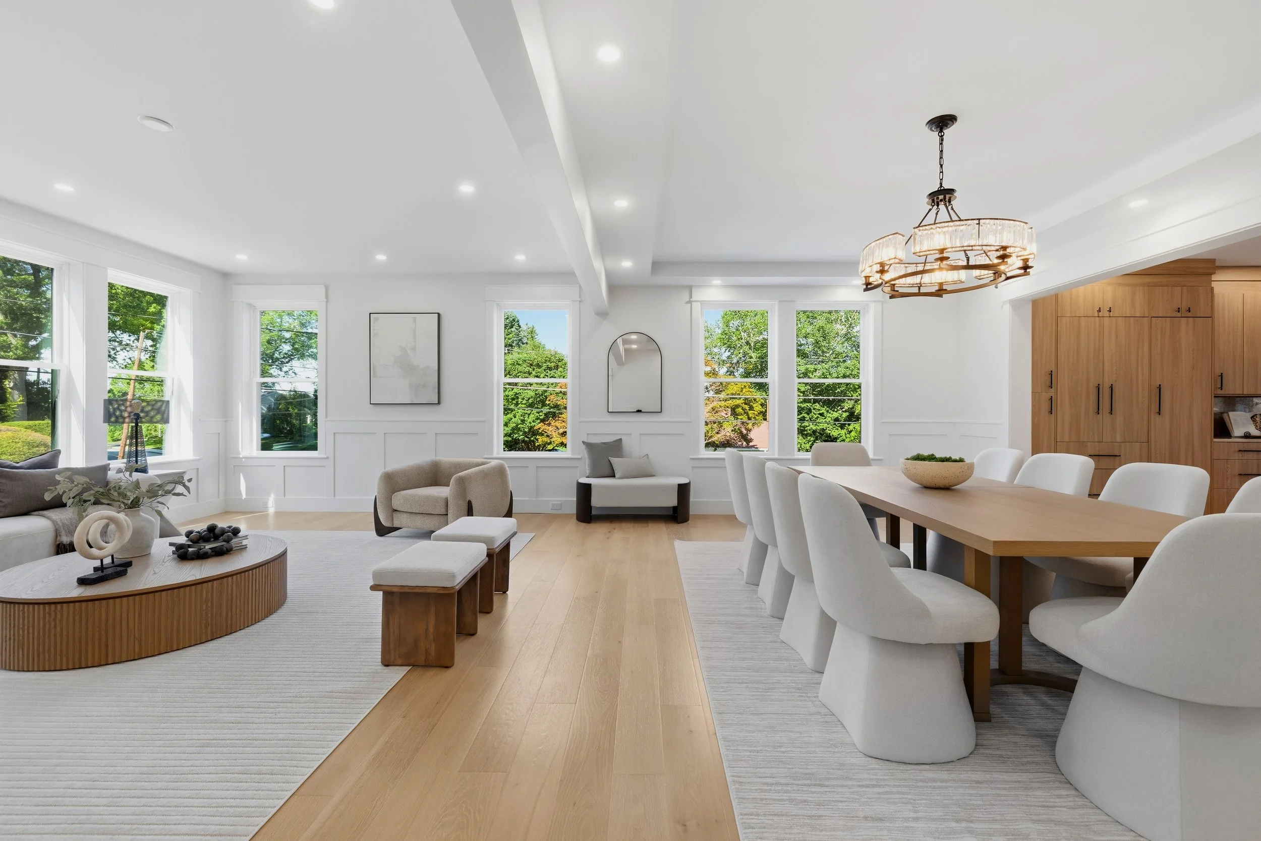 Bright living room with large windows, white walls, modern furniture, and a chandelier.