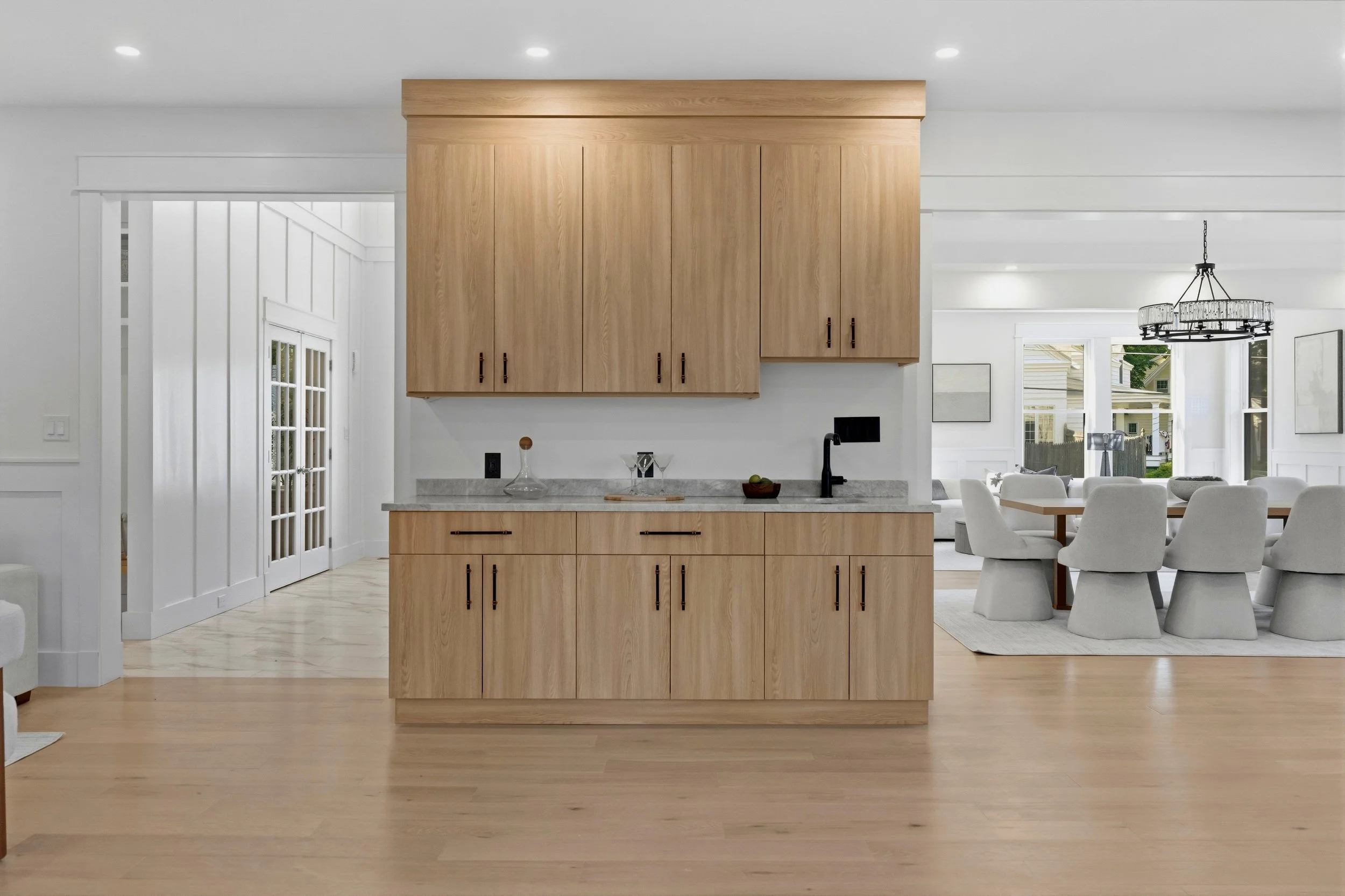 Open-concept kitchen and dining area with light wood cabinetry, white walls, and large windows.