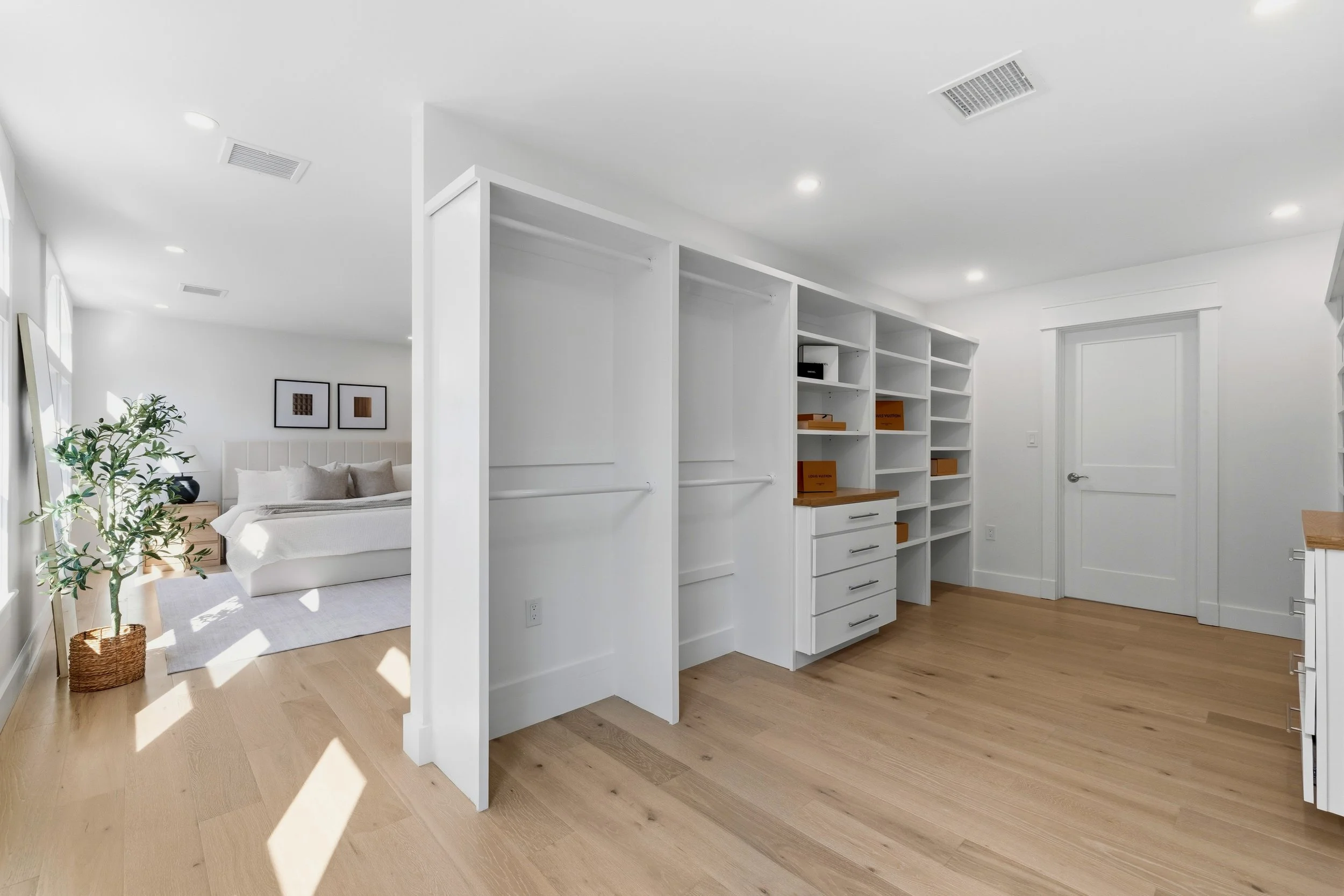 Empty white shelving unit in a room, with a door and hardwood floors visible, part of a modern, minimal living space with a bed and wall art in the background.