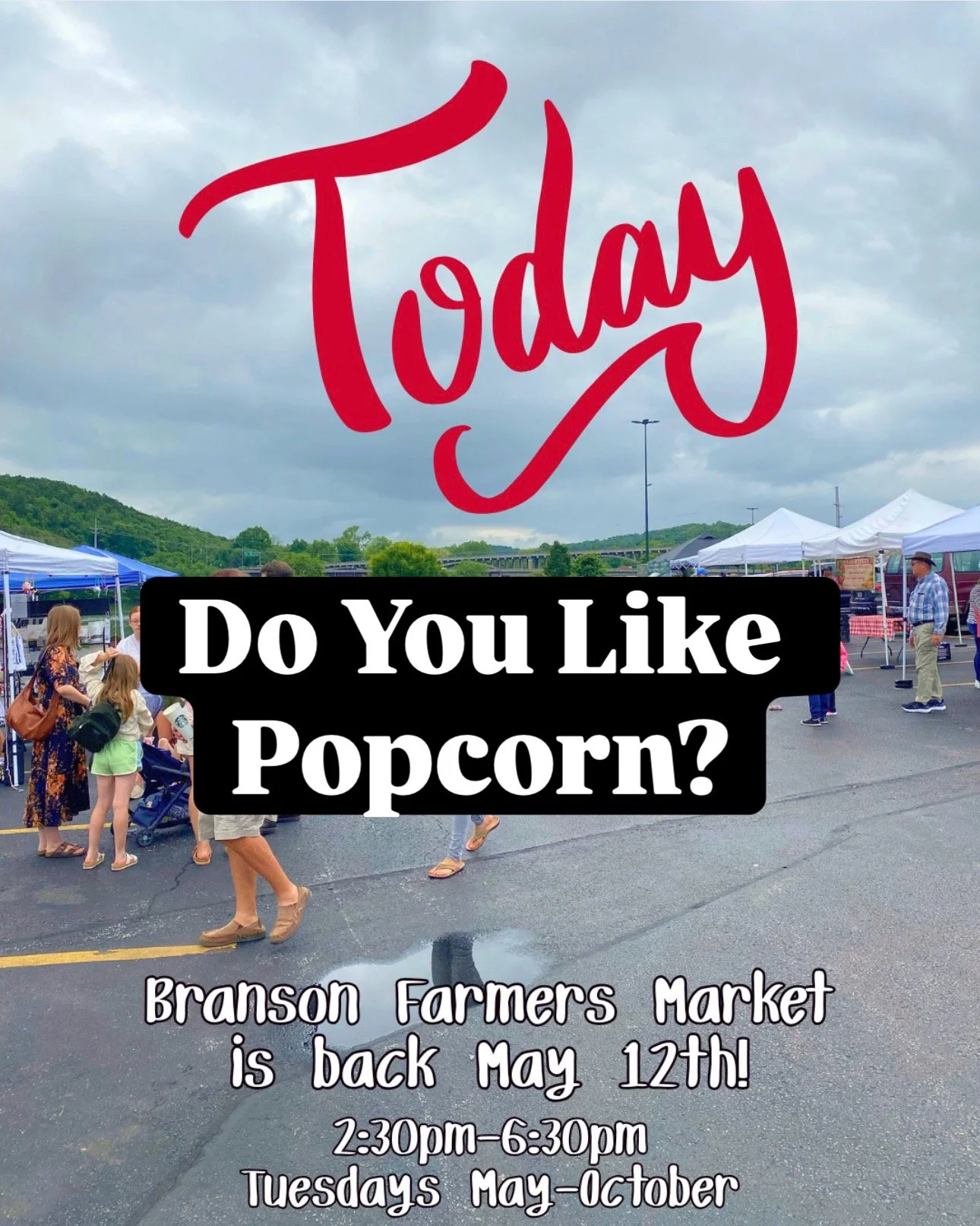 People walking and shopping at Branson Farmers Market in an outdoor parking lot, with tents and hills in the background, on a cloudy day.