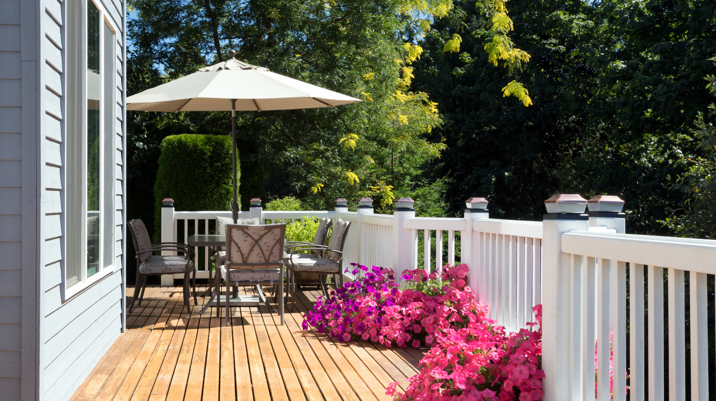 Backyard patio with outdoor dining setup, umbrella, and landscaping, showing a finished outdoor living space surrounded by greenery.