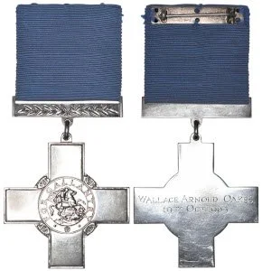 Two military medals, each with a blue ribbon and metal cross-shaped award, one with an emblem in the center and the other inscribed with 'Wallace Arnold Oakes 1935-2015'.