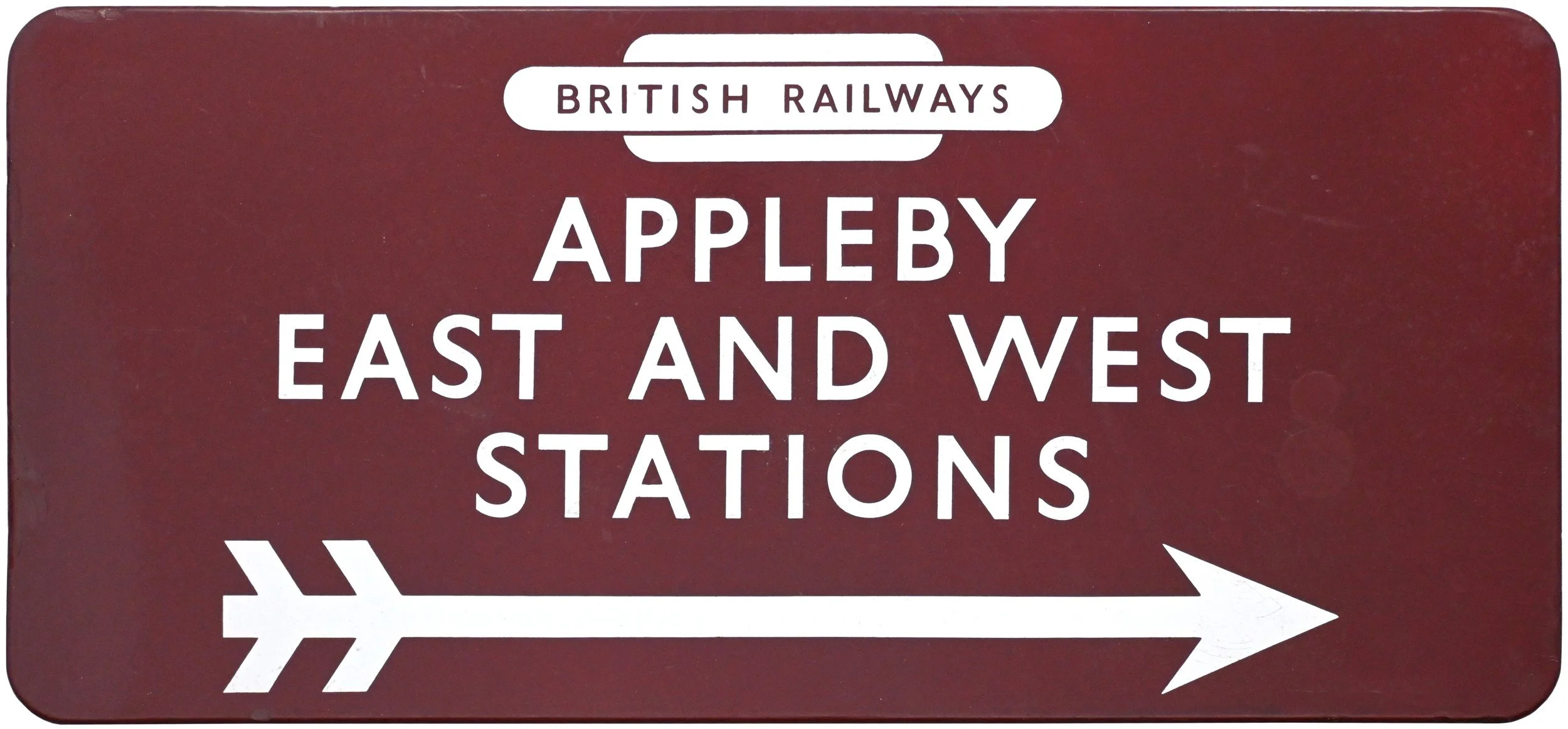 Sign with a maroon background and white text indicating directions for British Railways, pointing to Appleby, East and West stations, with a white arrow at the bottom.