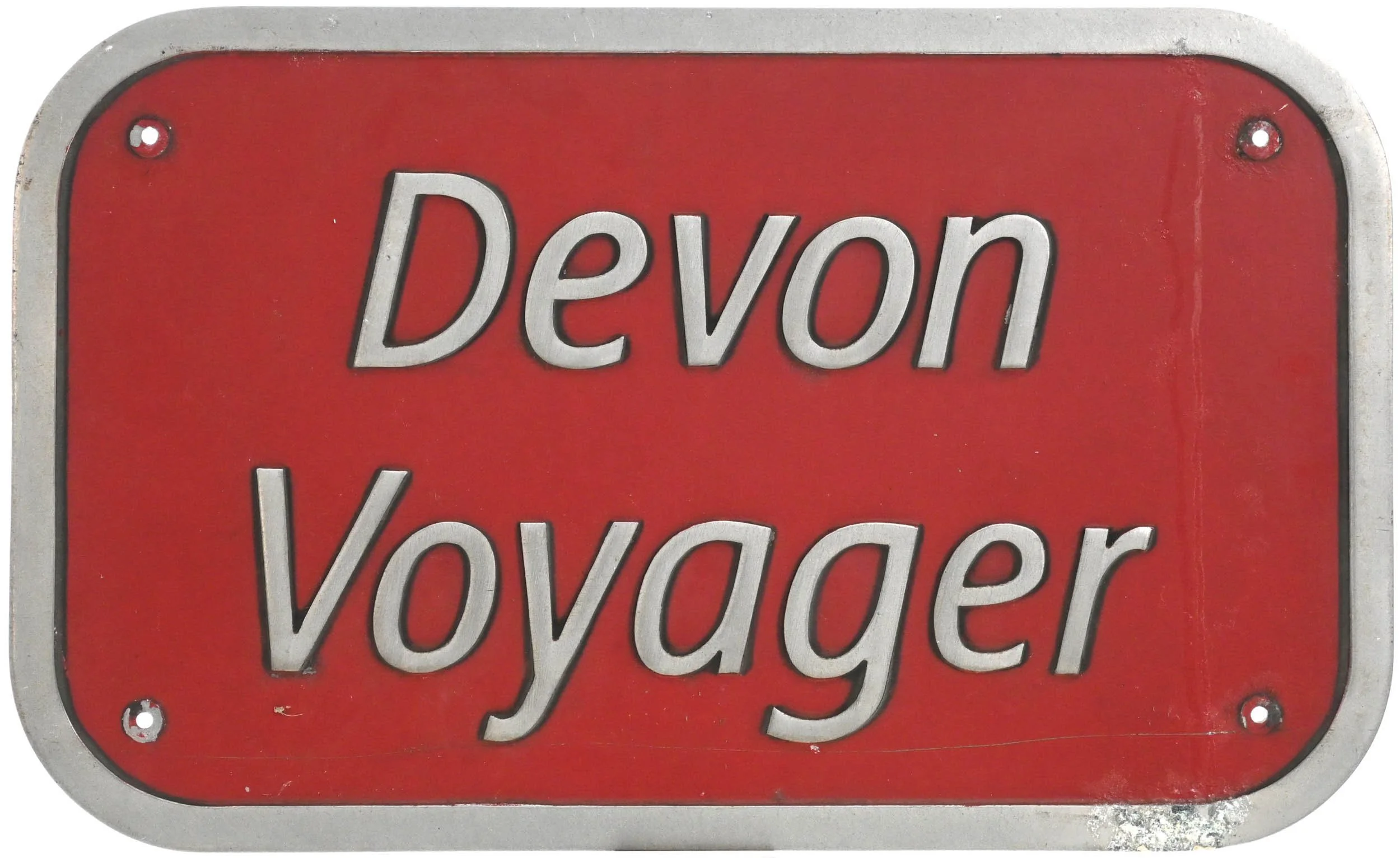 Red metal nameplate from a Virgin Voyager with silver border that reads 'Devon Vovager' in white letters.
