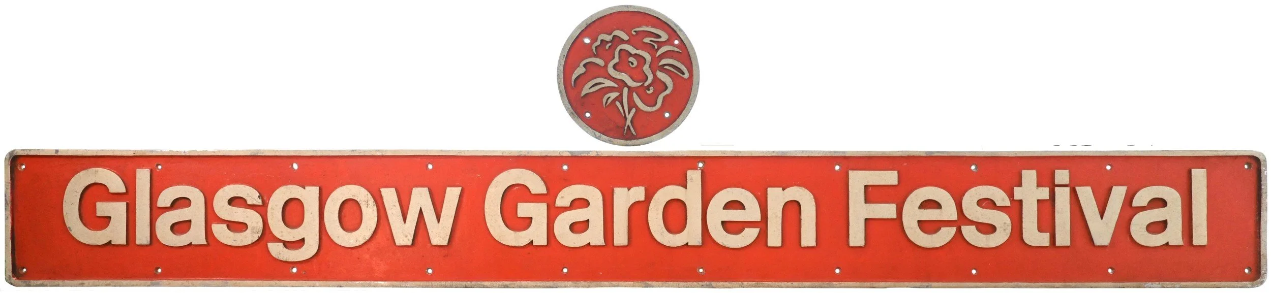 A rectangular red locomotive nameplate with beige text reading "Glasgow Garden Festival" and an emblem of a lion's head above.