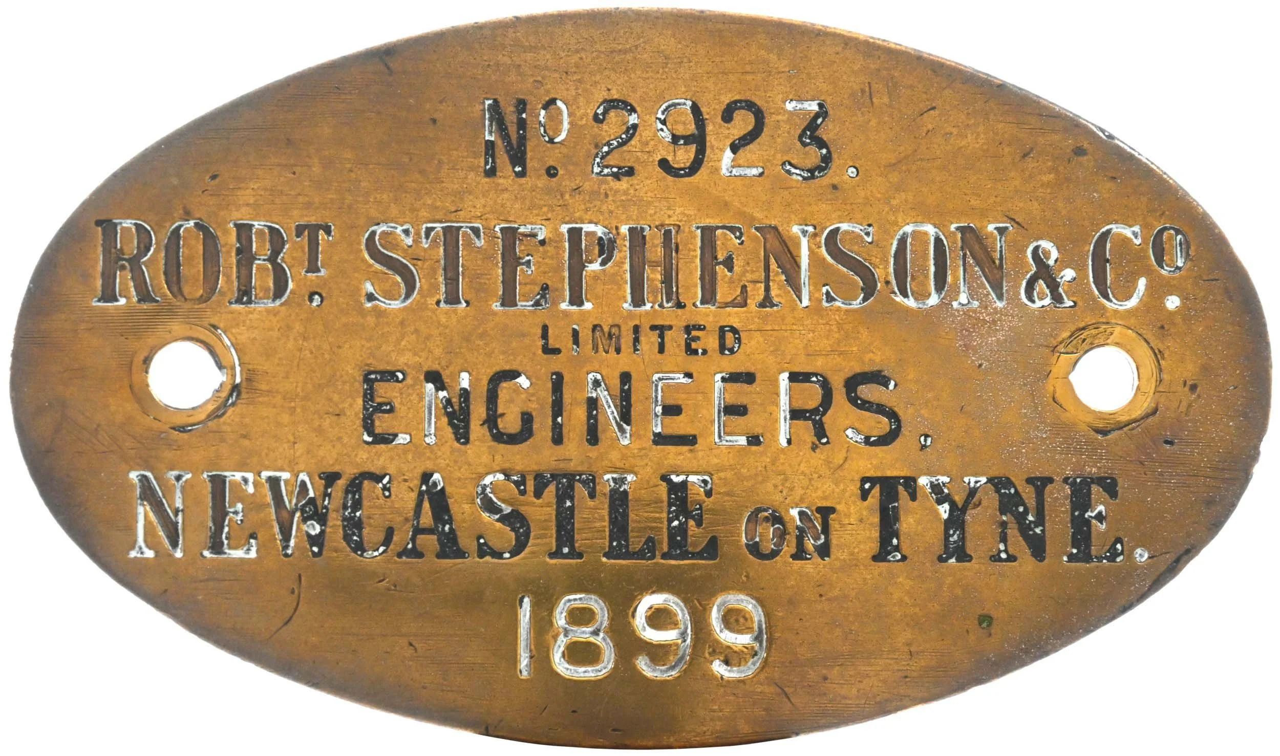 Brown oval metal identification tag with engraved text: 'N° 2923. ROBT. STEPHENSON & CO. LIMITED ENGINEERS, NEWCASTLE ON TYNE 1899'.