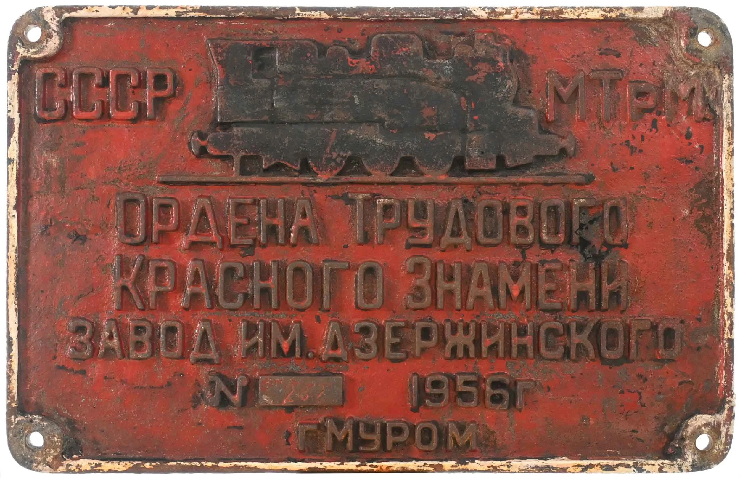 A rusted metal plaque with embossed Russian text and a map outline, red background with black and silver accents, worn edges, and four mounting holes.