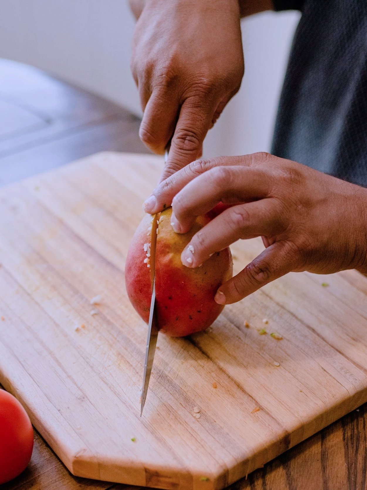 A person is cutting a red apple on a wooden cutting board with a knife.
