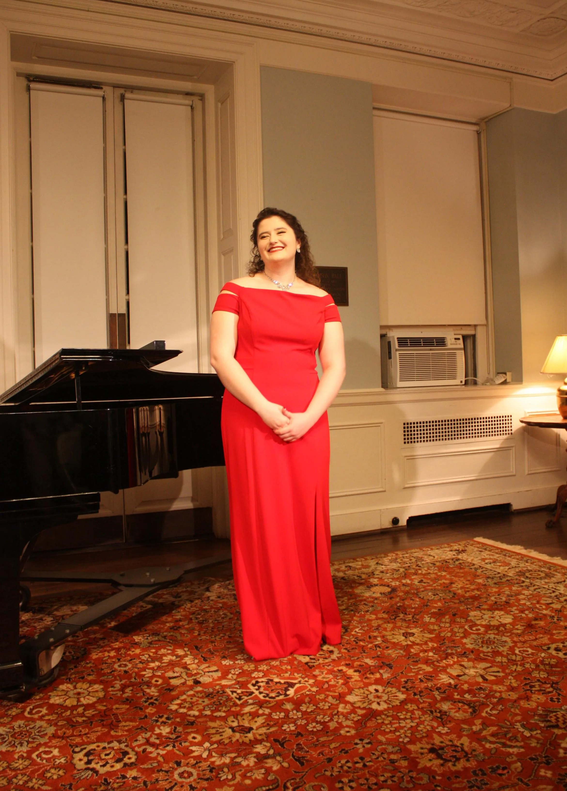 Amy Brandt, professional voice teacher and vocal coach standing beside a grand piano. Recital attire and performance