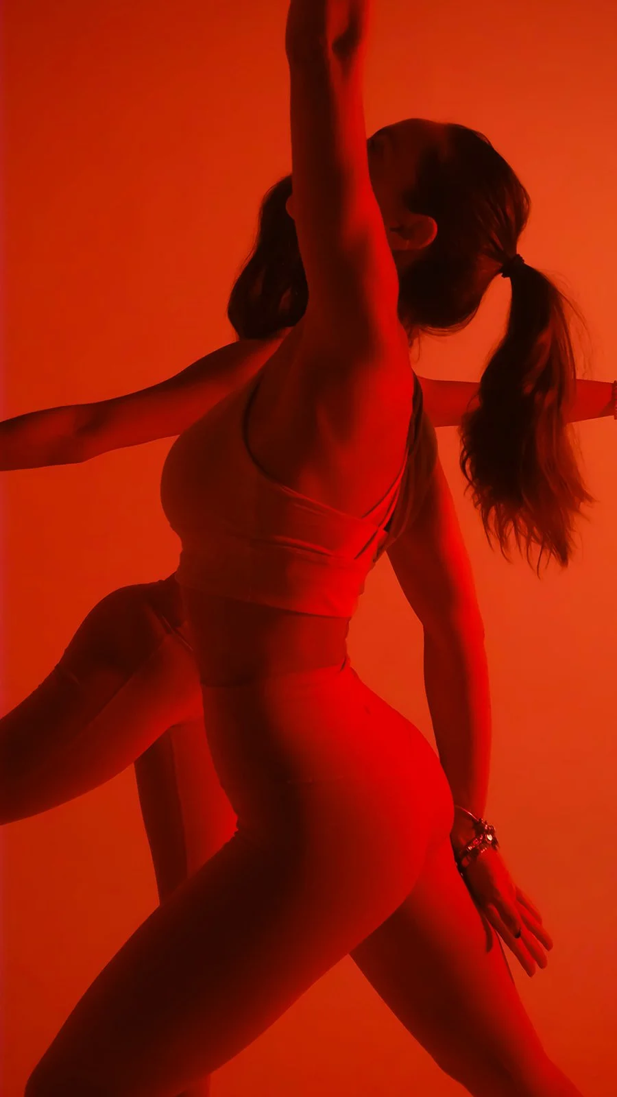 Person with long hair tied in pigtails practicing yoga or dance in red lighting.
