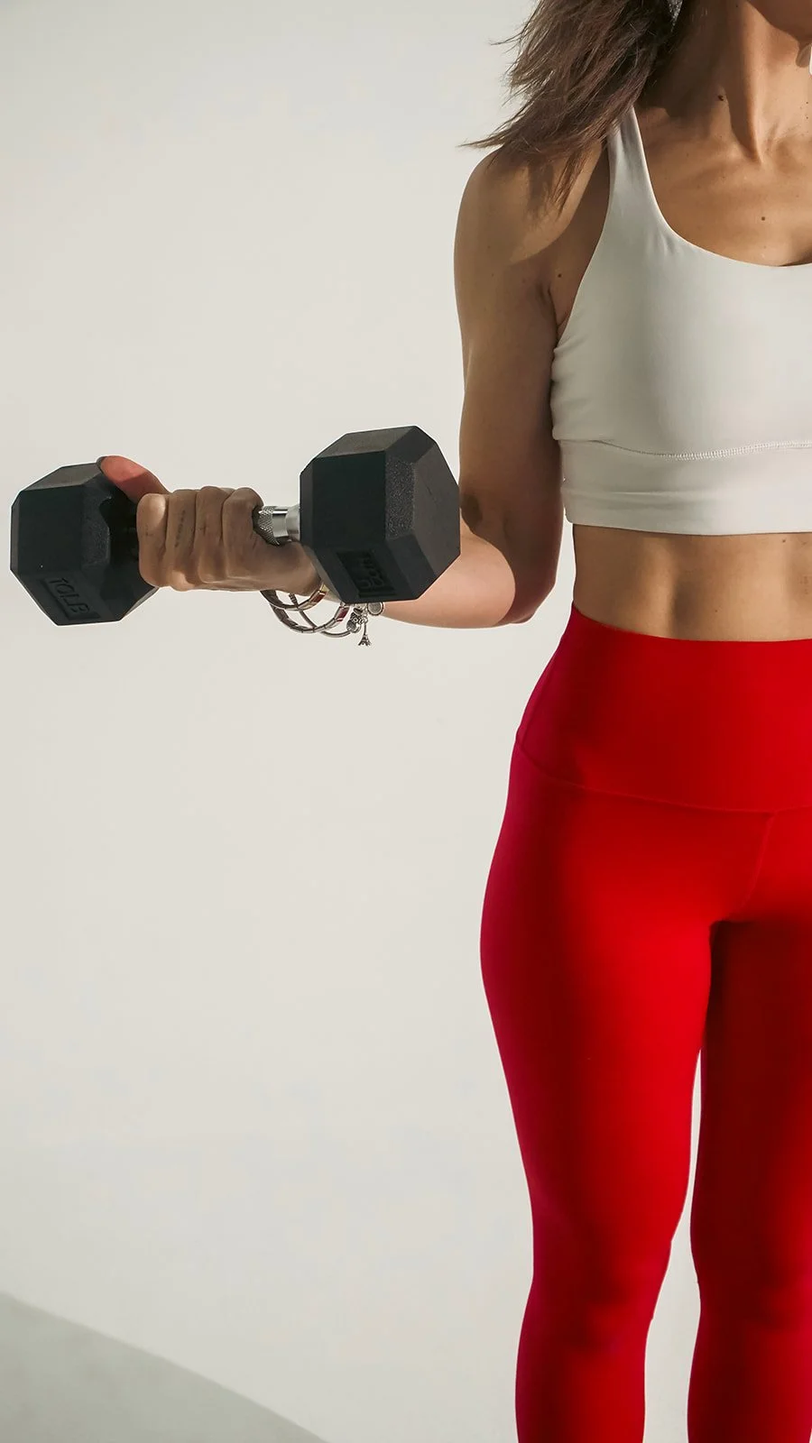 A woman wearing a white sports bra and red leggings holding a black dumbbell.