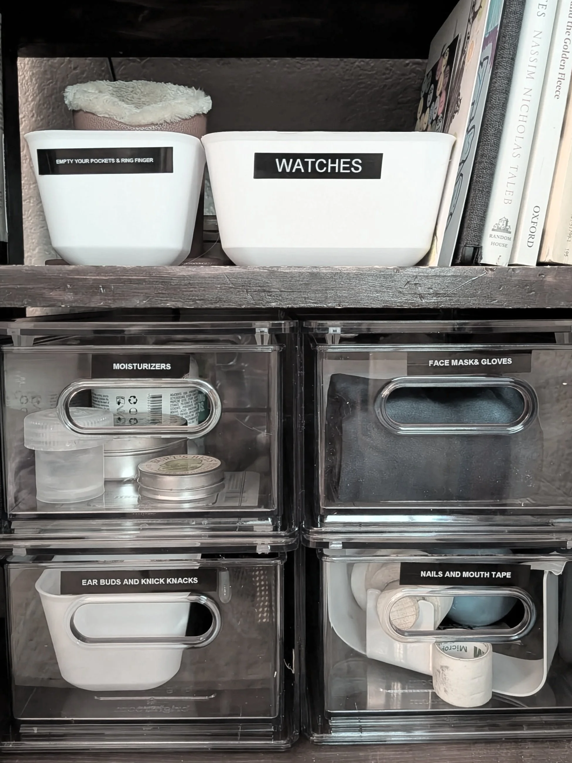 Home organization shelves with labeled containers for various small items and accessories, including watches, ear buds and knick knacks, nails and mouth tape, moisturizer, face mask, and gloves.