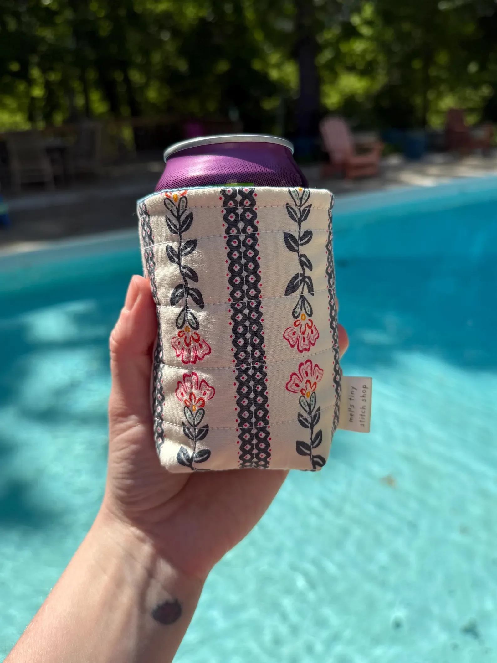 A hand holding a can in a hand-sewn koozie.