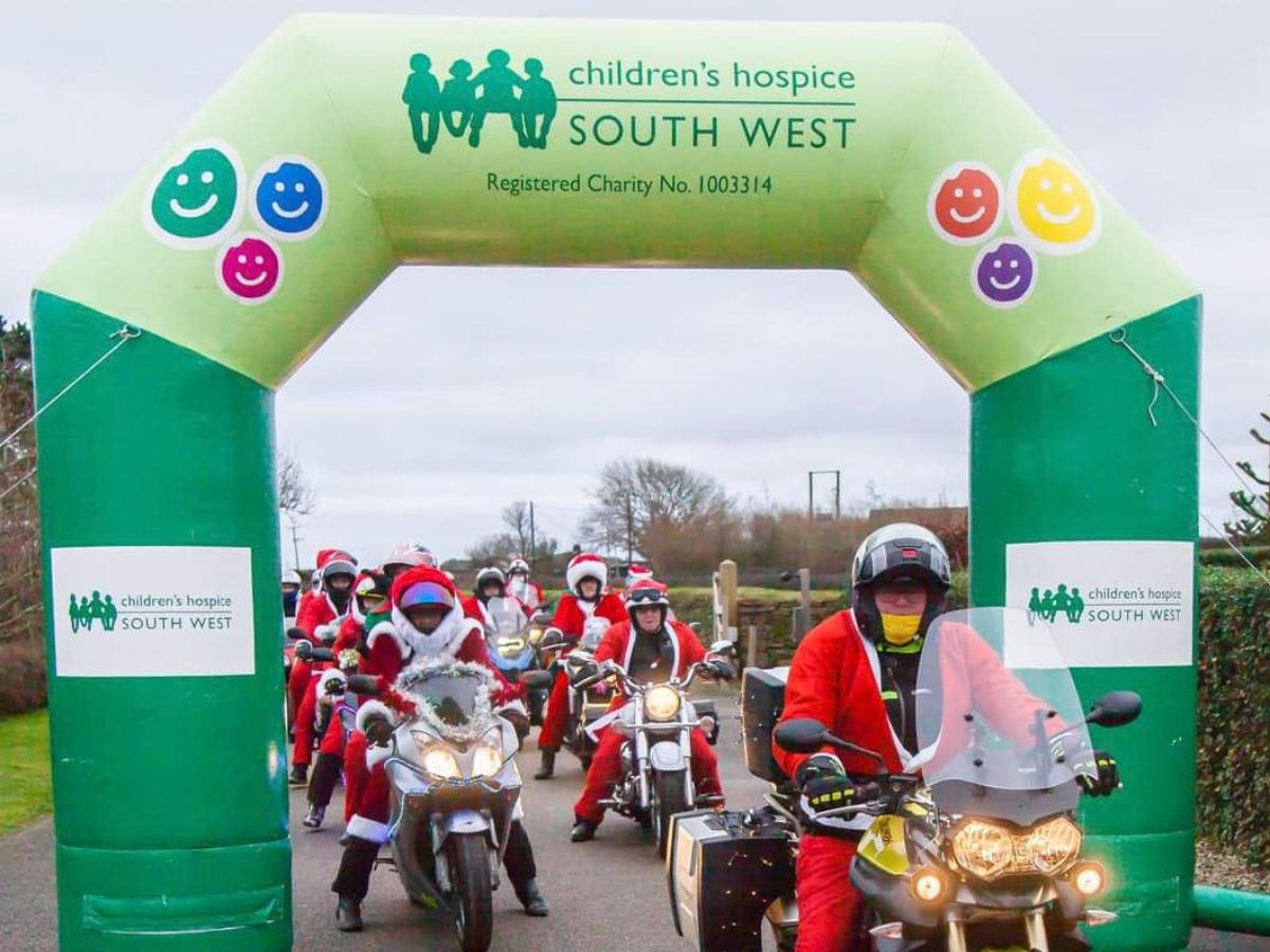 Santas on a bike riding through an archway labelled Children's Hospice South West