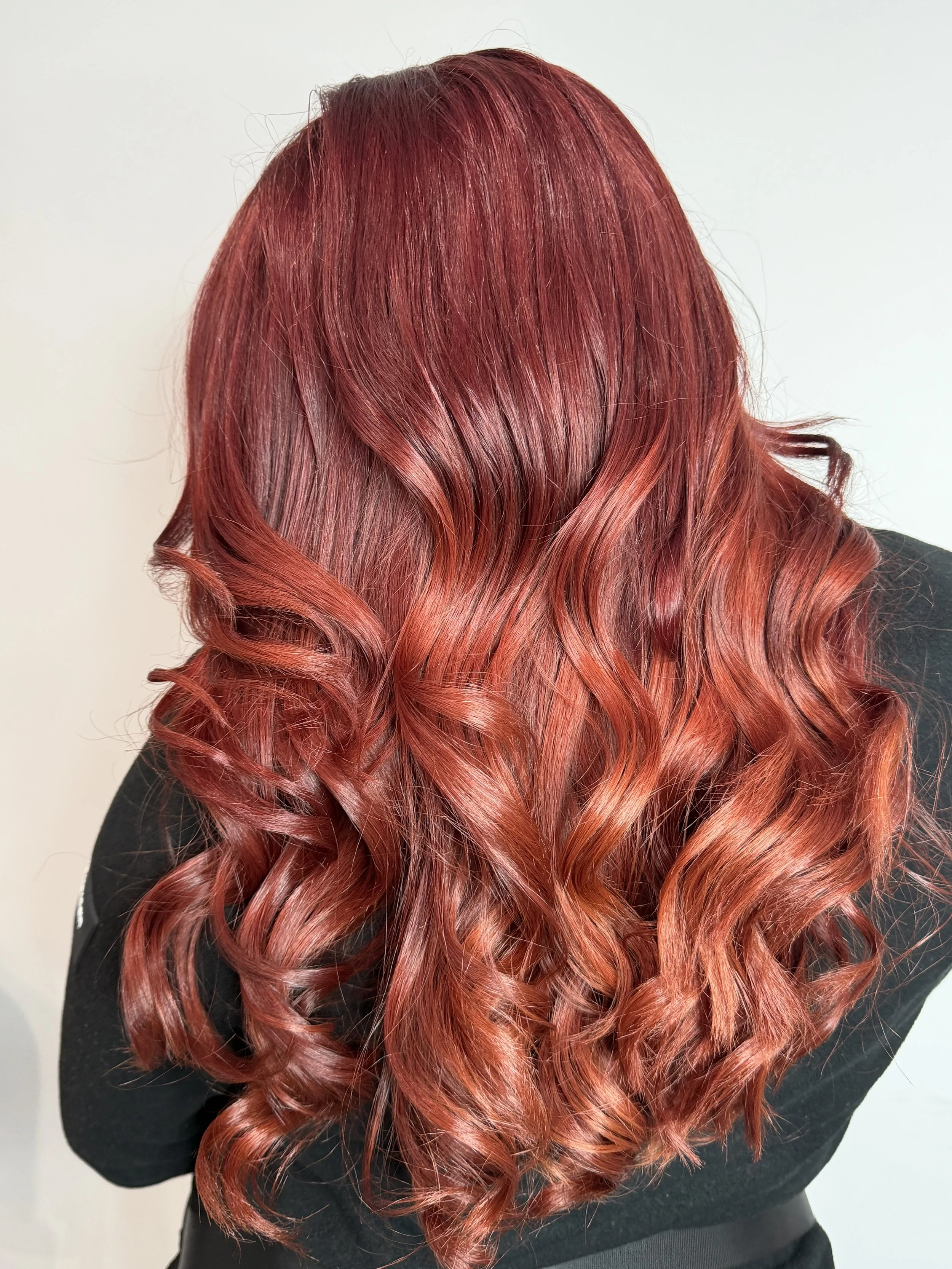 Back view of a person with long, wavy hair dyed in shades of red and orange.