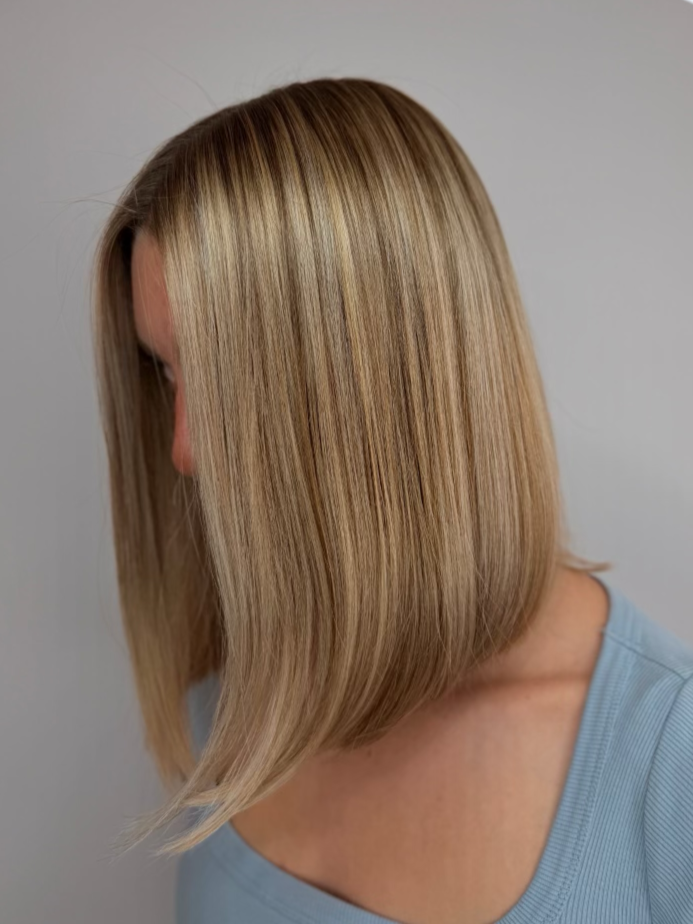 Woman with straight, shoulder-length blonde hair, wearing a light blue shirt, facing side with head slightly bent down.