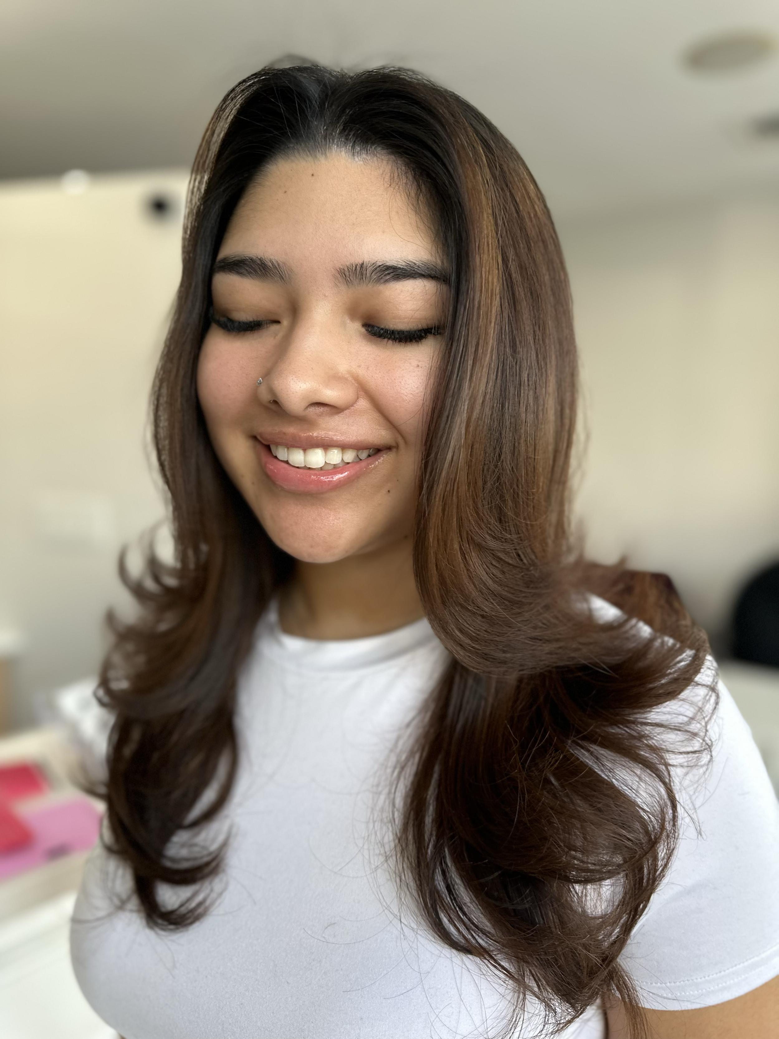 Close-up of a woman with long, curly brown hair, smiling gently and wearing a white shirt.