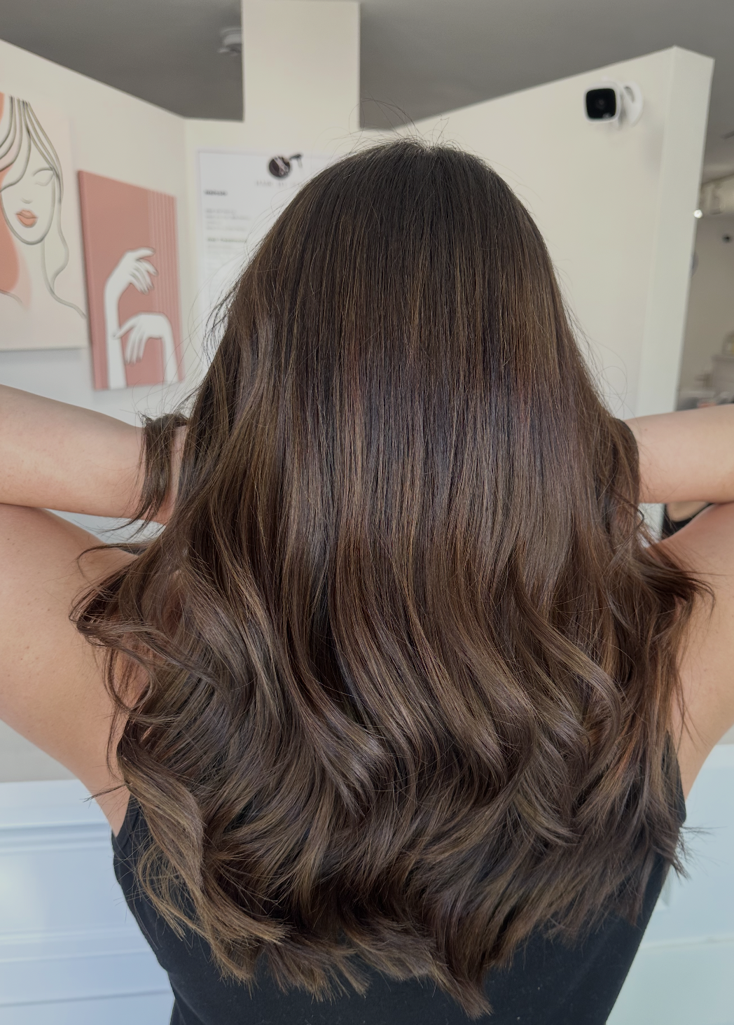 Back view of a woman with long, wavy brown hair in a salon or similar setting.