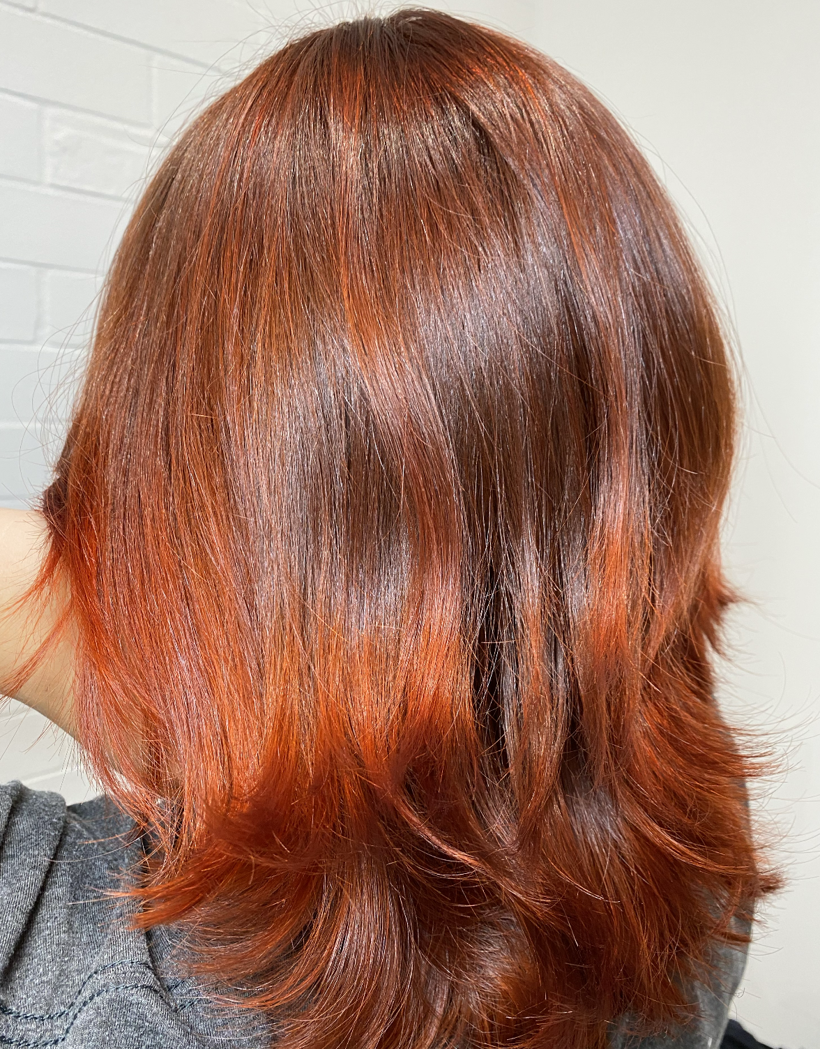 Back of a person's head with shoulder-length, vibrant red hair styled in loose waves.