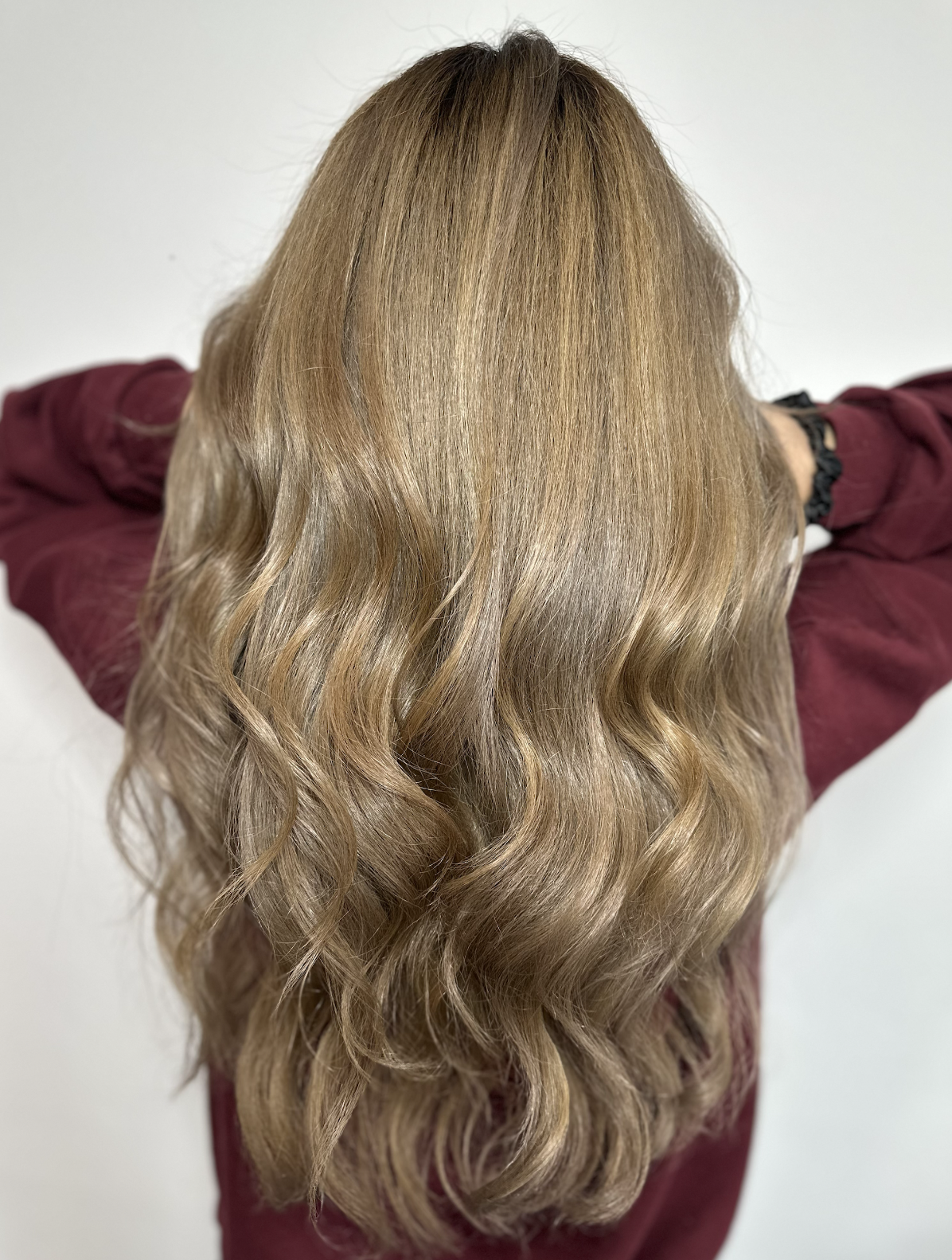 Back view of a woman with long, wavy, light brown hair wearing a burgundy top.
