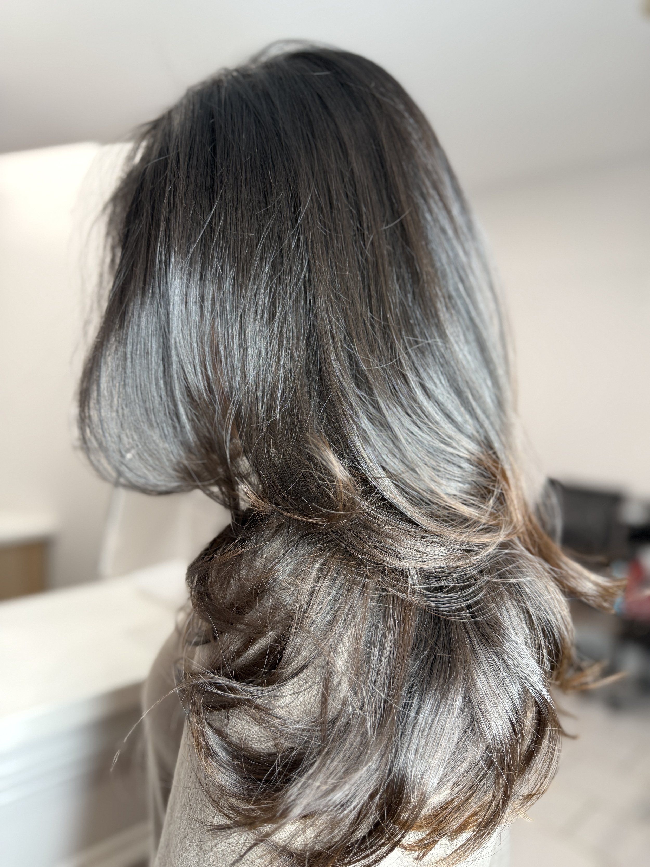 A close-up of a hairstyle featuring dark brown to gray ombre hair with loose waves.