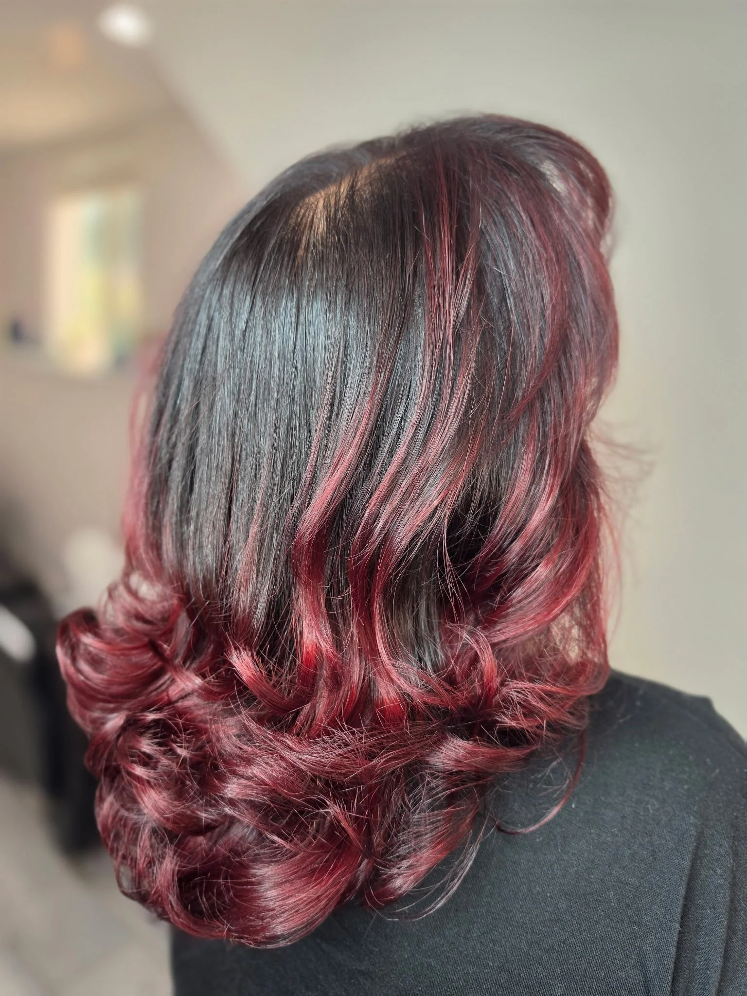 A person with long, wavy hair dyed in shades of black, gray, and vibrant pink, styled in loose curls.