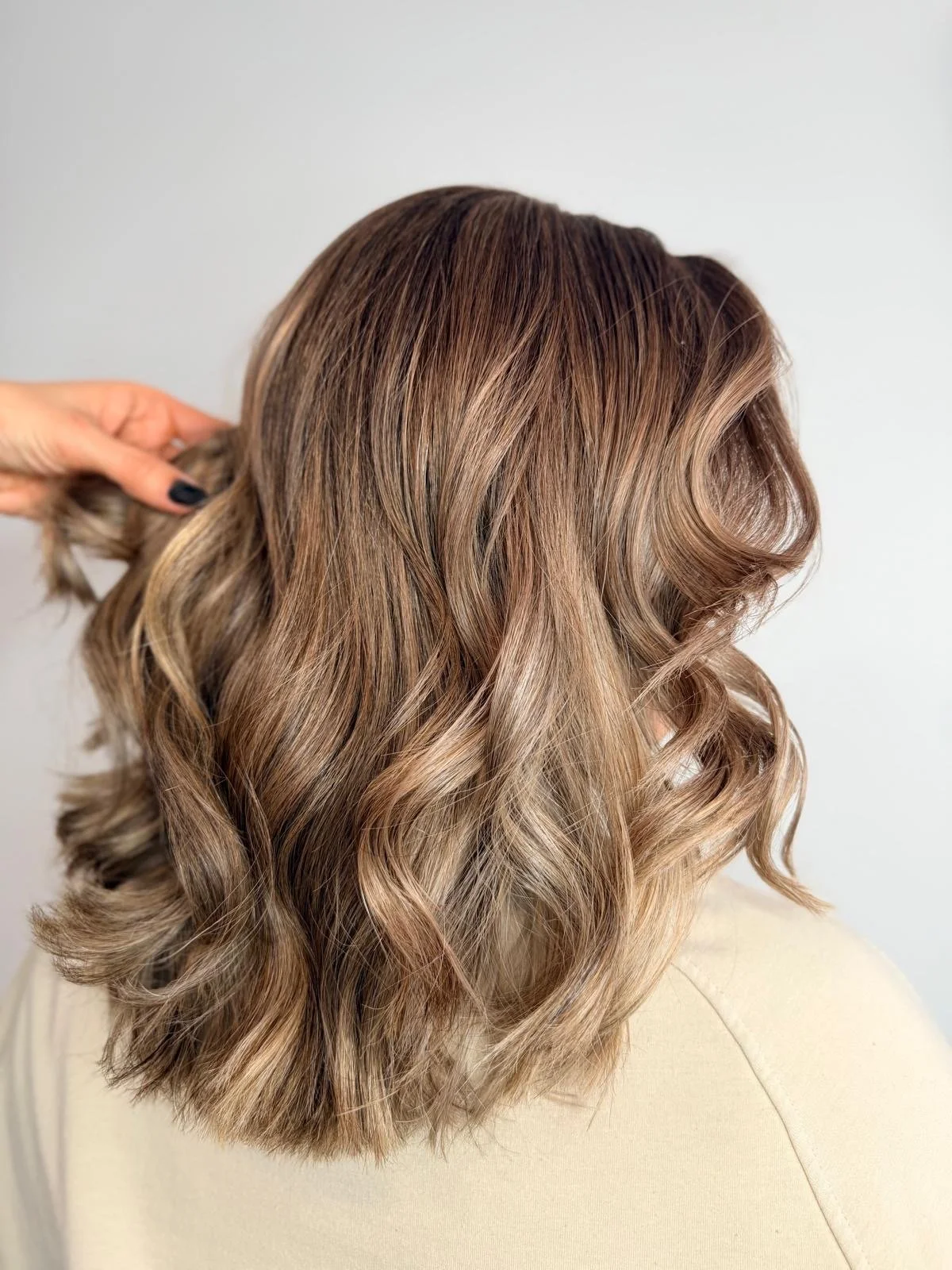 Side view of a woman's hair with warm brown and blonde balayage curls.