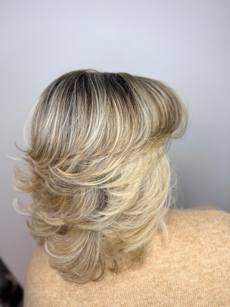 A woman with shoulder-length, layered, blonde hair styled with soft waves