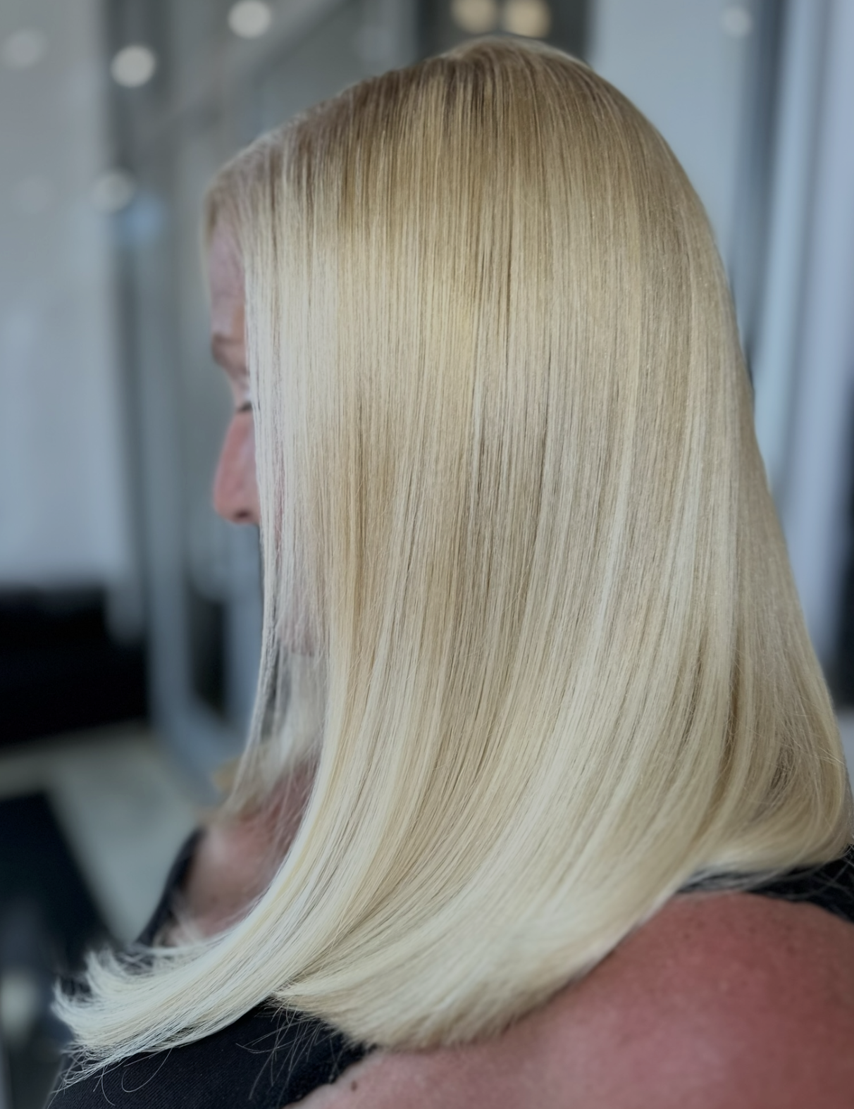 A woman with long, straight, blonde hair sitting in a salon chair, getting her hair styled.