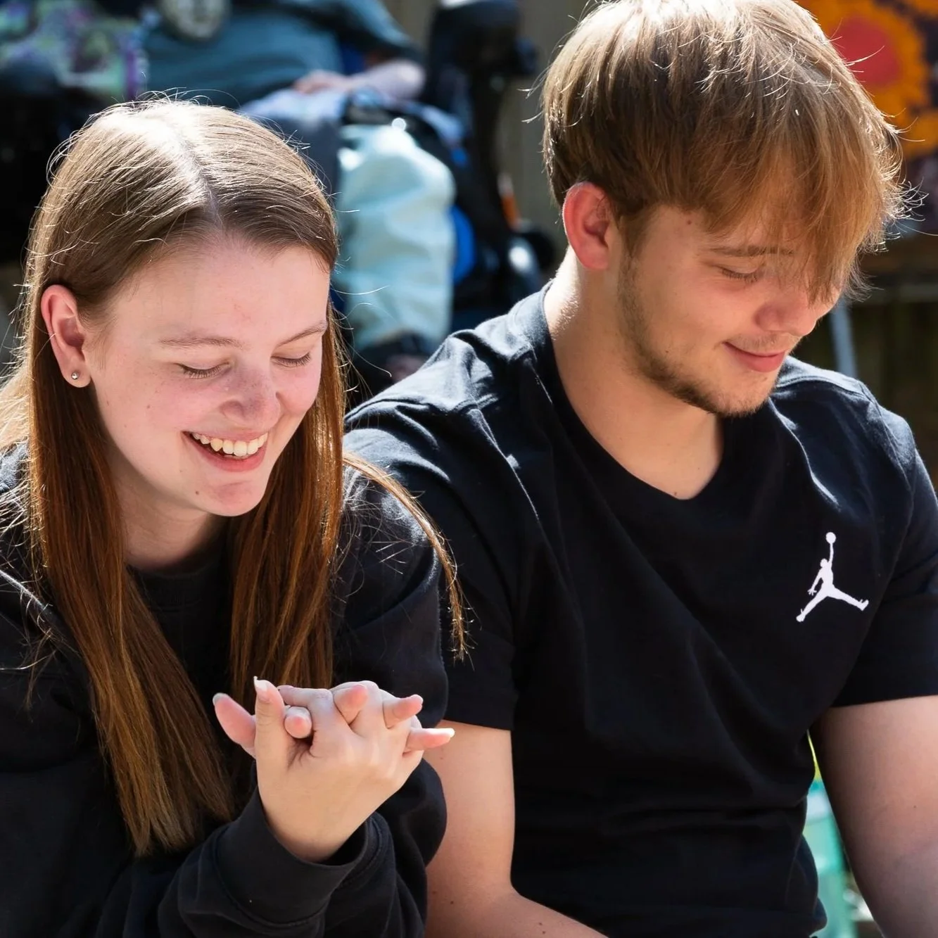 A young woman and young man sitting close together outdoors, smiling and enjoying each other's company.