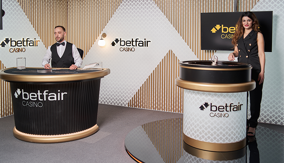 Casino dealers at Betfair Casino, with two women standing behind separate blackjack tables, in a modern, decorated room.