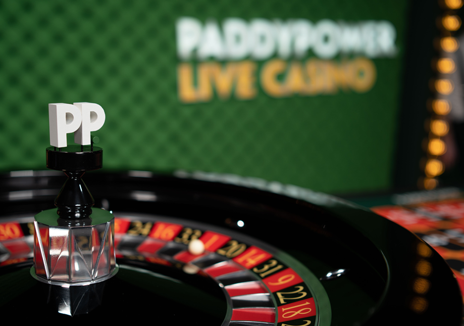 Close-up of a roulette wheel at Paddy Power live casino with a chip marked 'PP' on a stand in the foreground and a green backdrop with Paddy Power branding.
