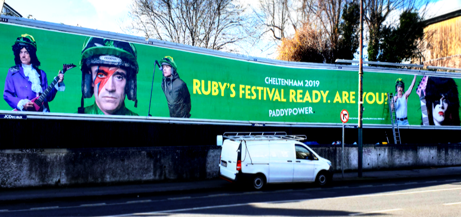 Large green banner advertising Cheltenham 2019 festival with images of musicians and performers, featuring the message "Ruby's Festival Ready. Are You!" by Paddy Power.