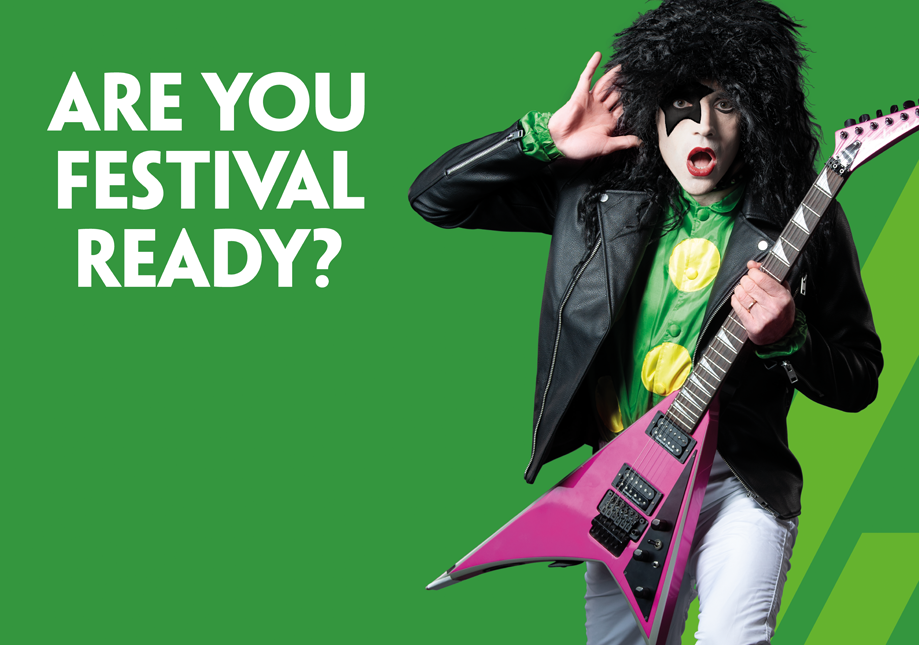 Person dressed as a guitarist with a black curly wig, face makeup, and a black leather jacket, holding a pink electric guitar against a green background with text saying "Are You Festival Ready?".