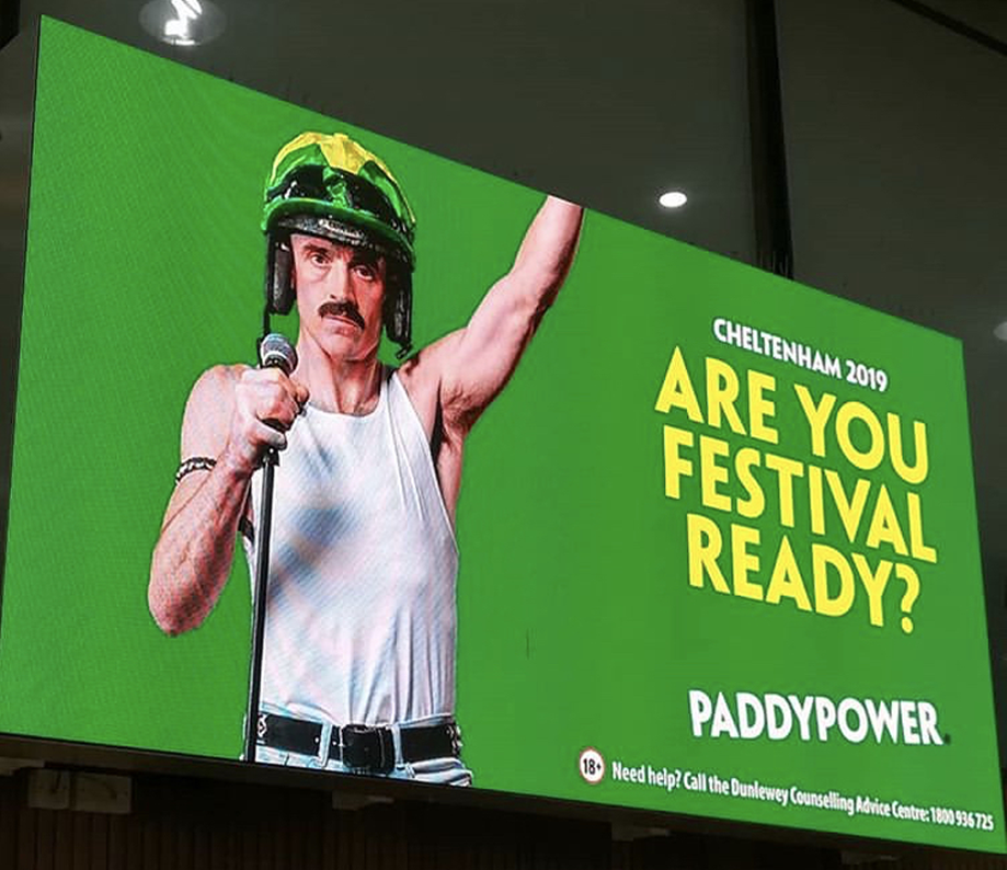 Bill Murray wearing a helmet and tank top, holding a microphone, promoting the Cheltenham 2019 event with the slogan "Are You Festival Ready?" on a green background.