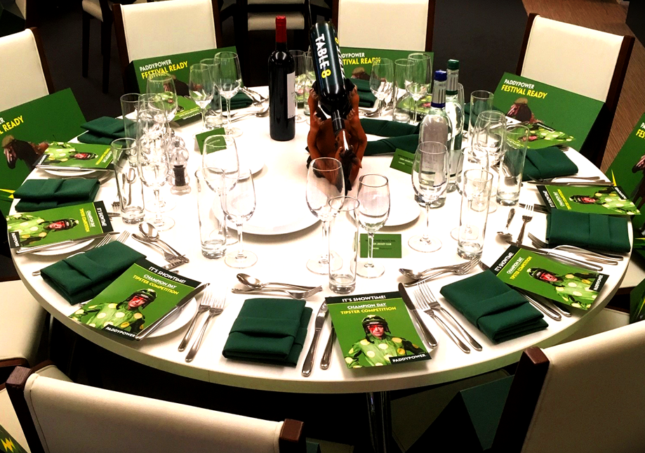 Round table set for a celebration with green-themed decorations, multiple glasses, green napkins, and a centerpiece featuring a small statue.
