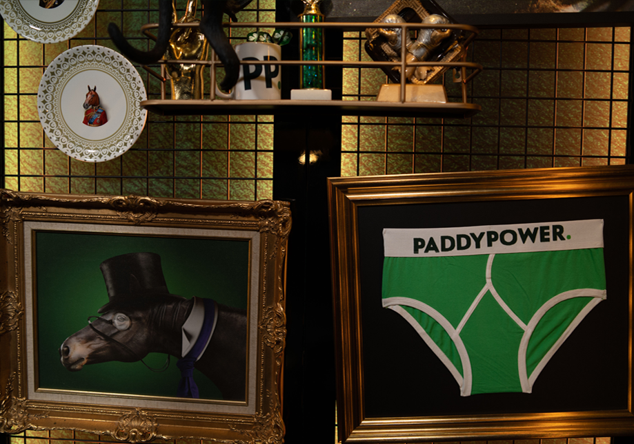 Decorative shelves with a plate featuring a horse, a mug with the word "PUPPY," and a model of a skull. Framed artwork of a goat wearing a top hat and glasses, and green underwear with the brand name "PADDYPOWER."
