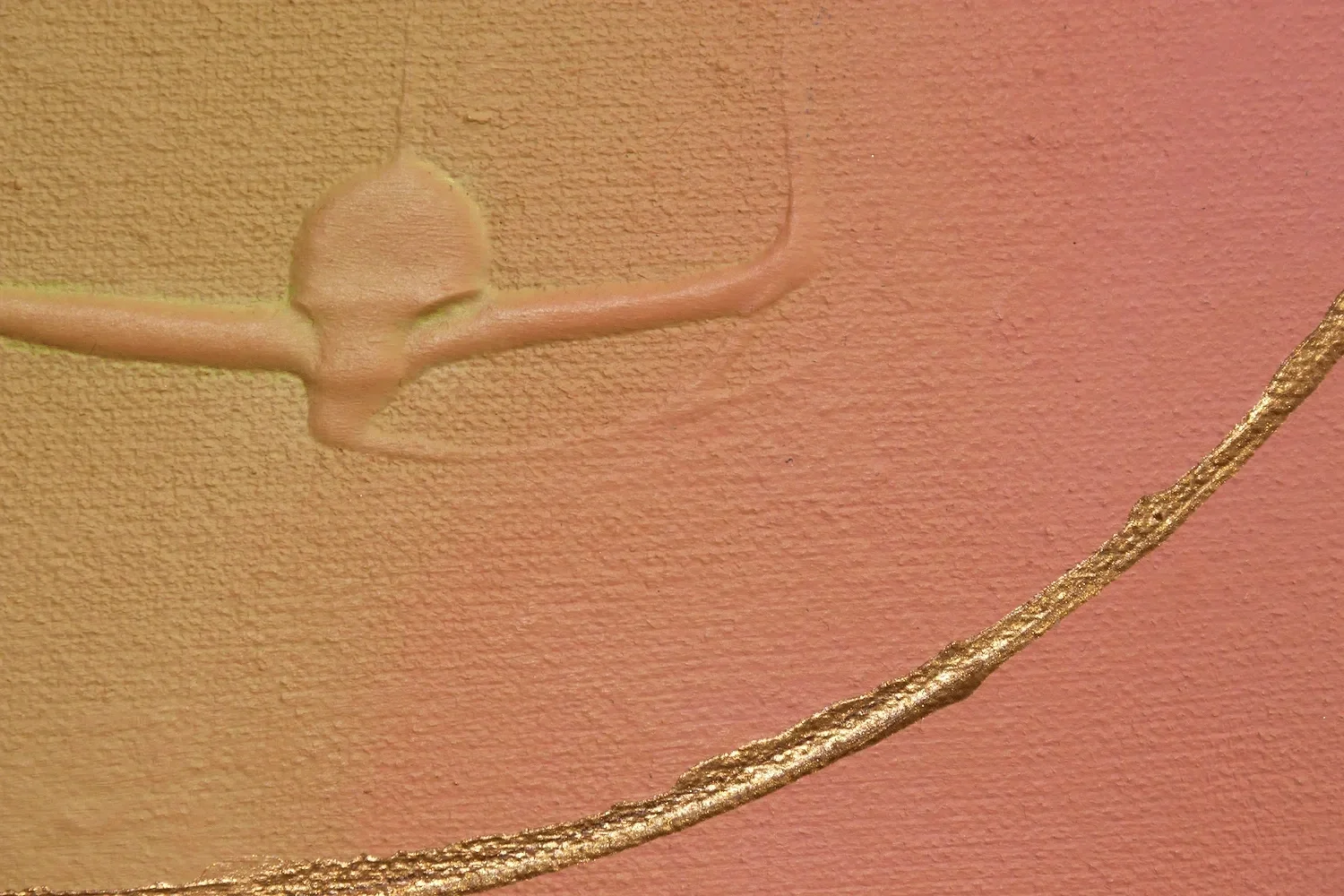 Nahaufnahme einer Wand mit einer 3D- Stuckdekoration in Form eines Engels und einer goldenen Zierleiste auf einem rosa- beigen Hintergrund.