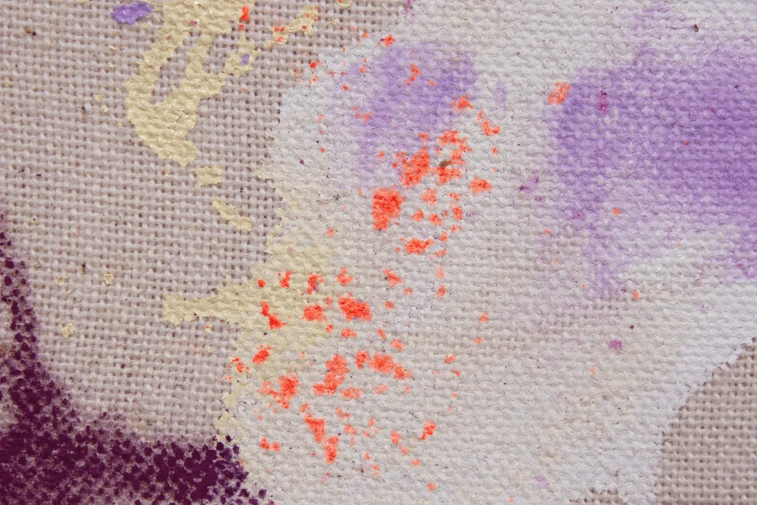 Nahaufnahme eines Stoffes mit Farbspritzern in violett, orange und beige. Das Gewebe ist sichtbar und die Farben sind verteilt, wodurch ein abstraktes Muster entsteht.