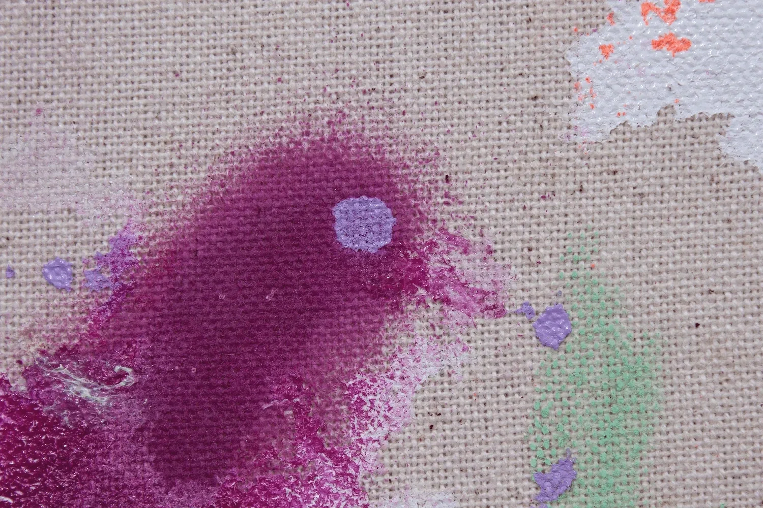 Farbspritz auf Leinwand mit Farben in Lila, Pink, Grün und Orange.