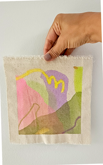 Hand hält ein kleine bemalte Leinwand mit abstrakten Farben und Formen gegen eine weiße Wand.